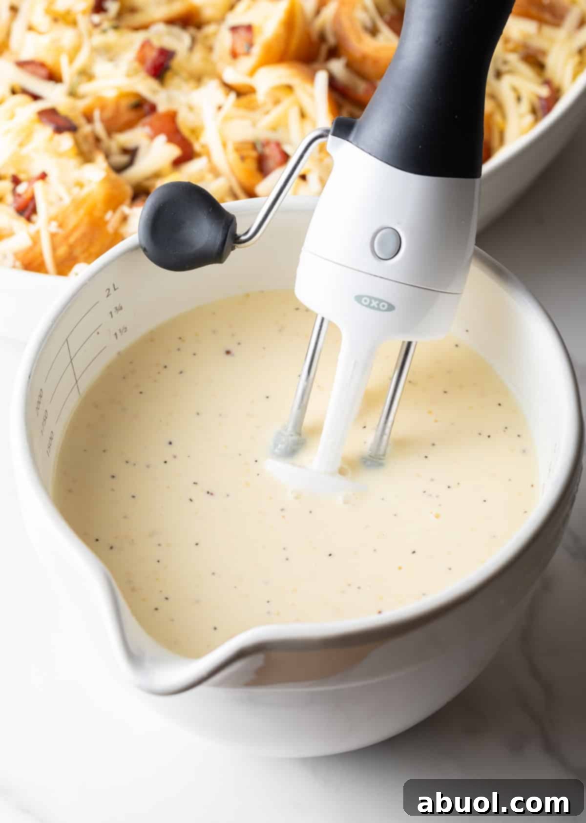 Cream, eggs, and mustard are being mixed together with a hand mixer in a white mixing bowl.