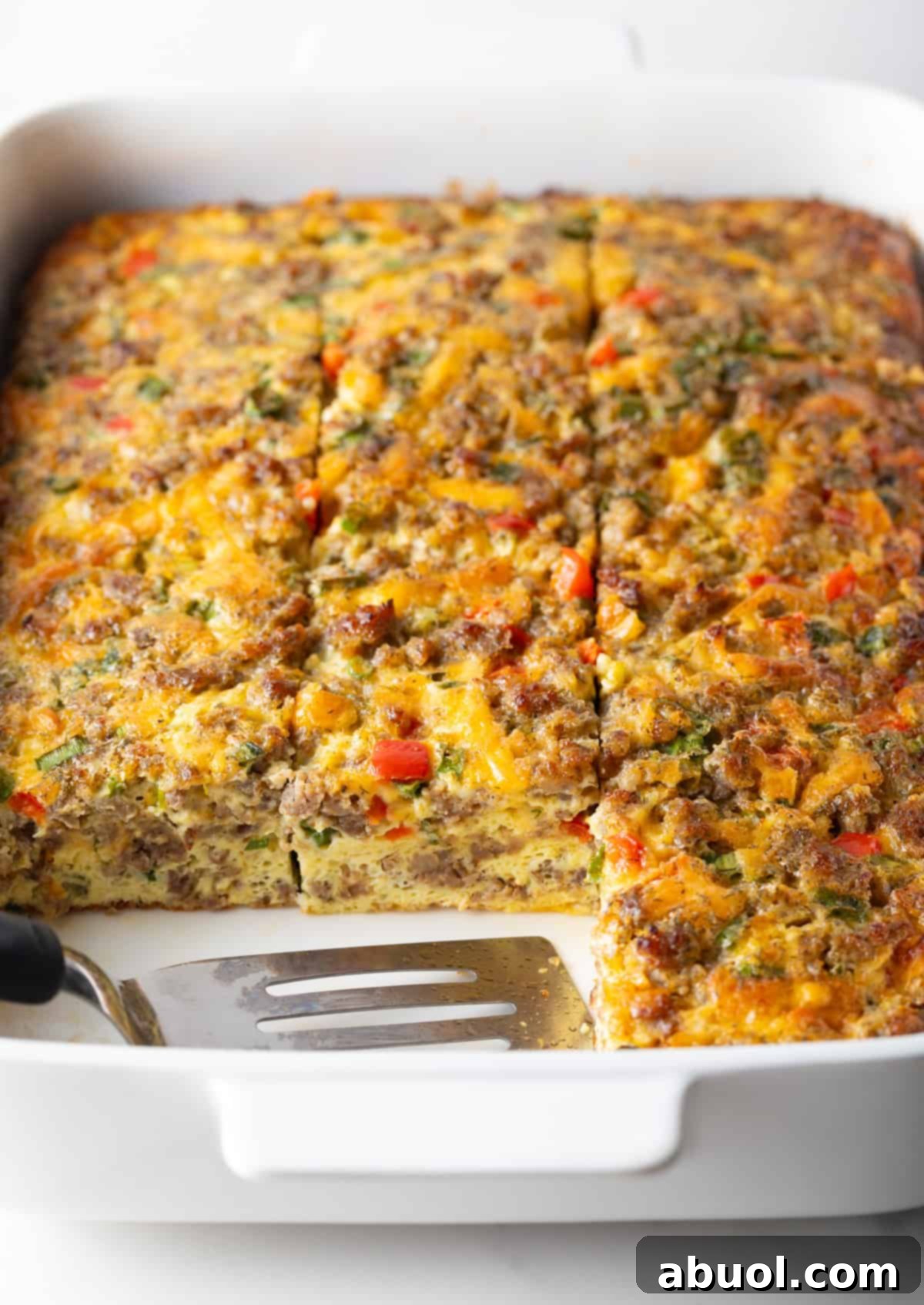 Pan of egg casserole with sausage and veggies. A spatula is in the pan, with square portions of the casserole removed.