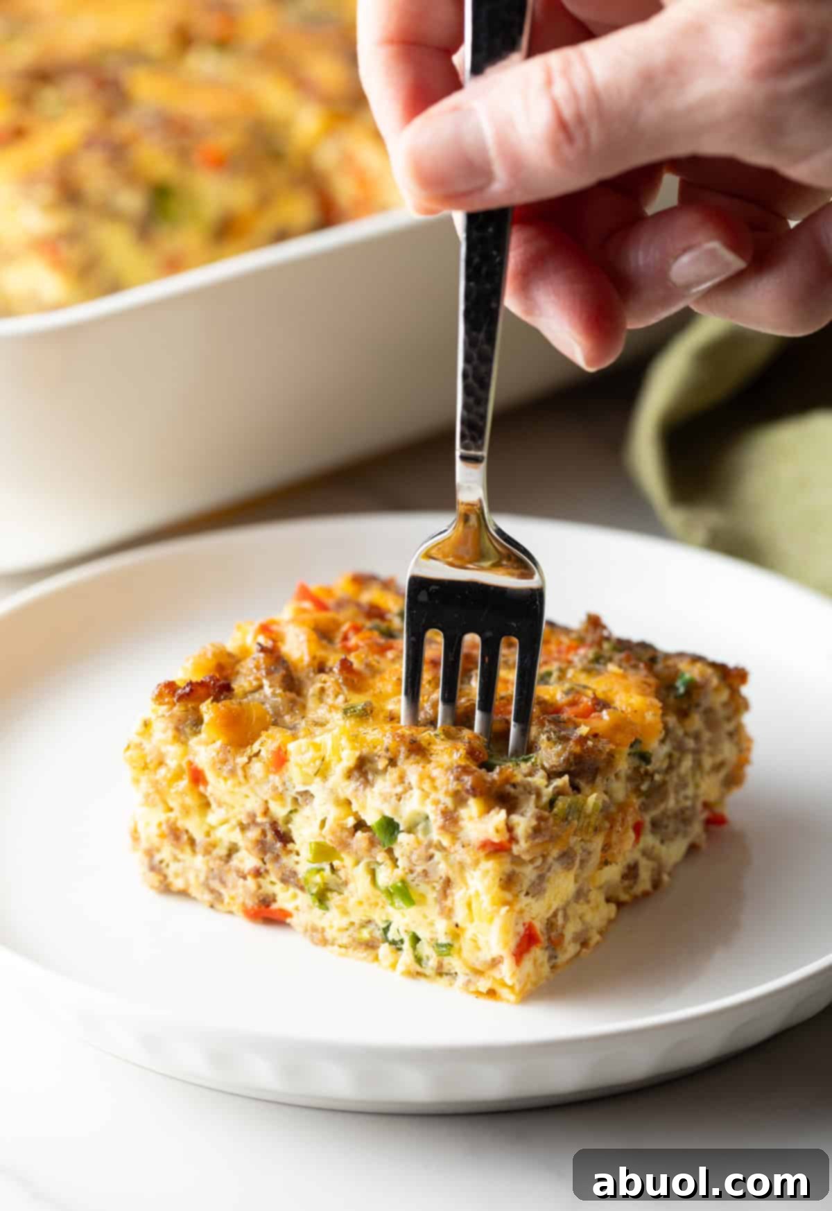 Fork taking a section from a square of sausage breakfast casserole on a white plate
