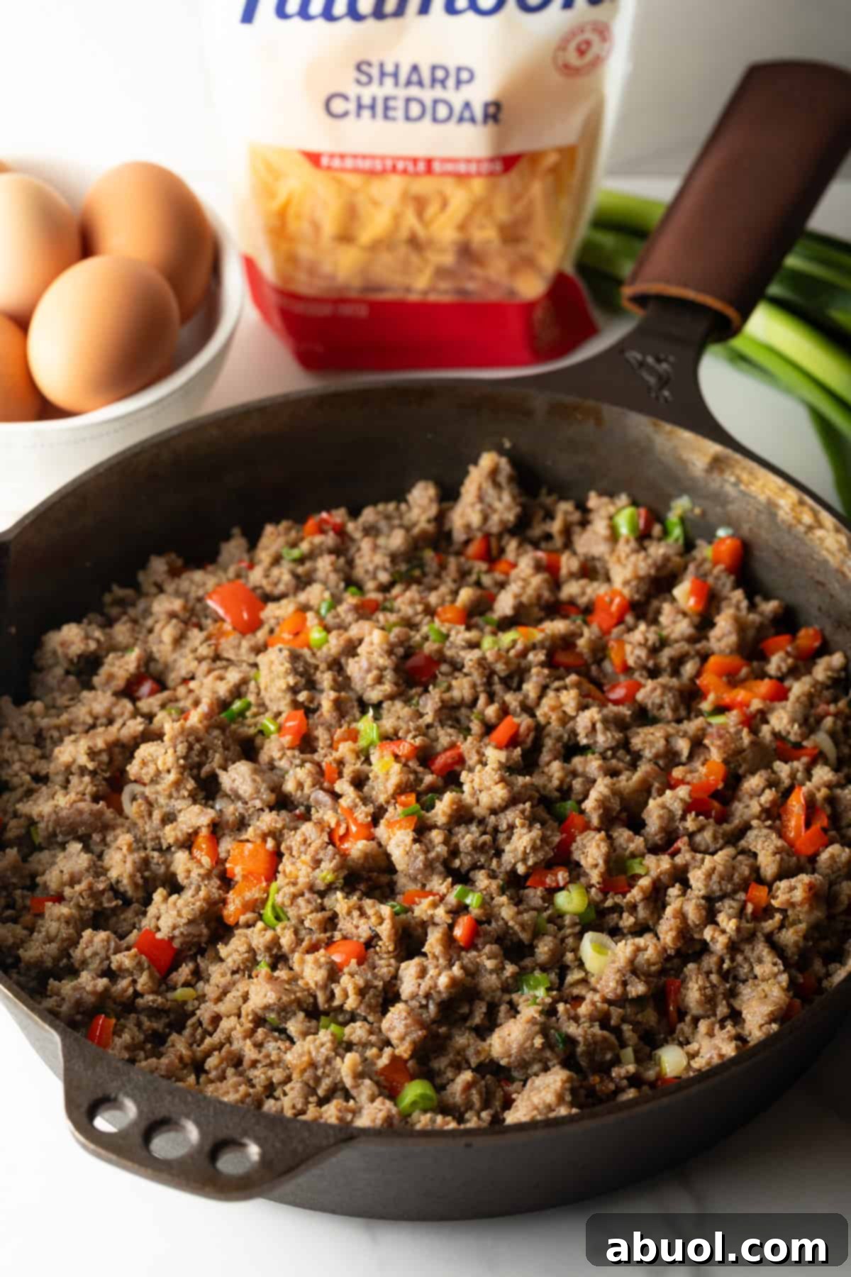 Cooking ground sausage in a cast iron skillet with diced red peppers