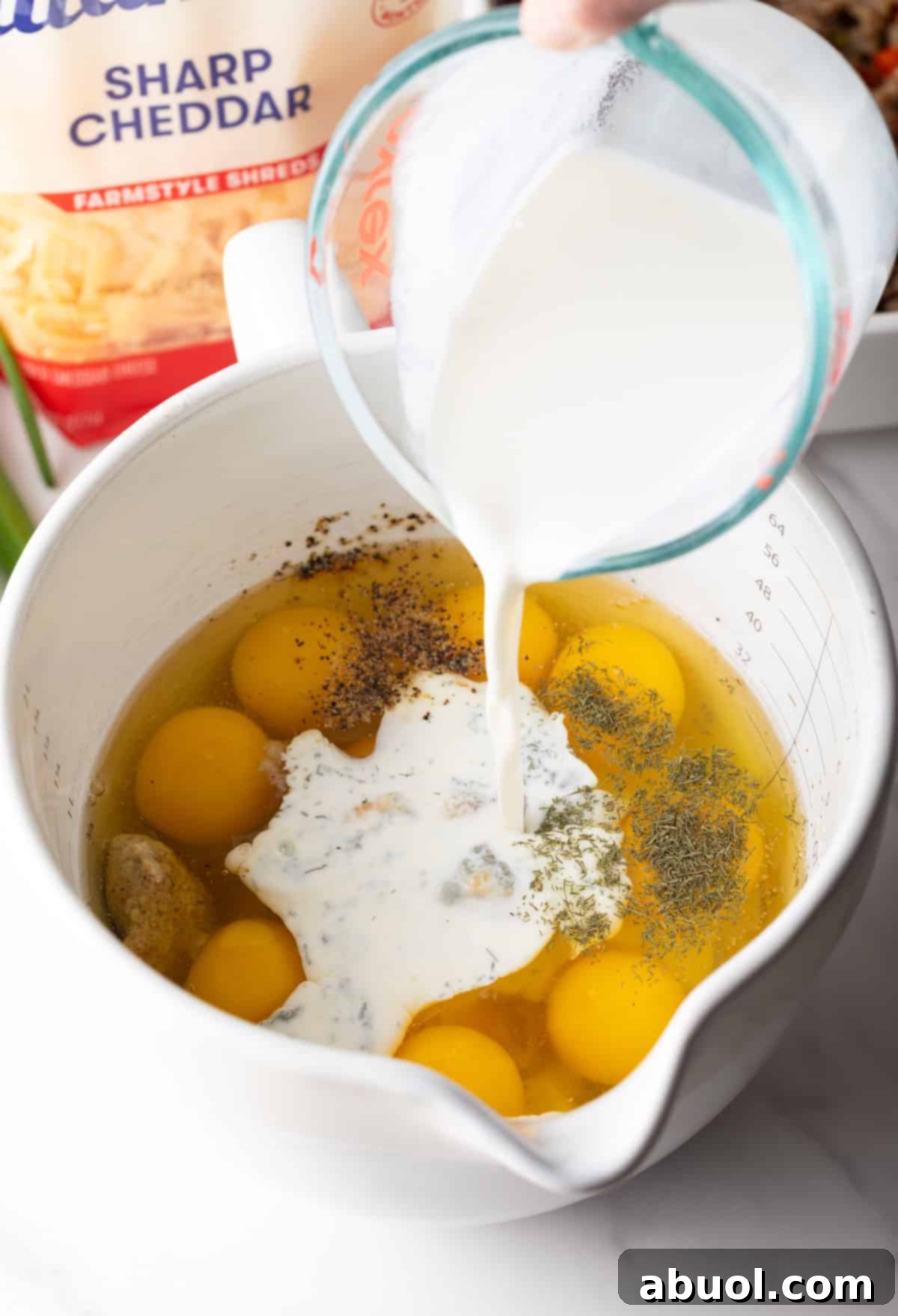 Adding milk to raw eggs in a white measuring pitcher