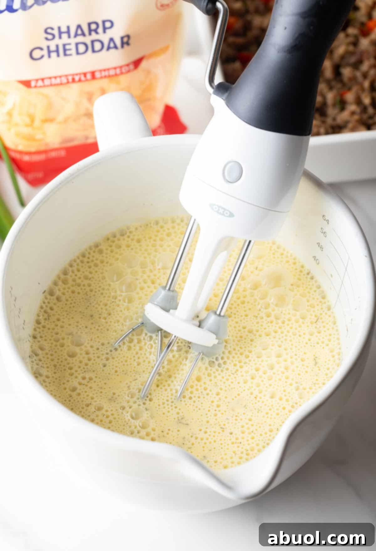 Hand mixer blending eggs and spices in a white measuring pitcher