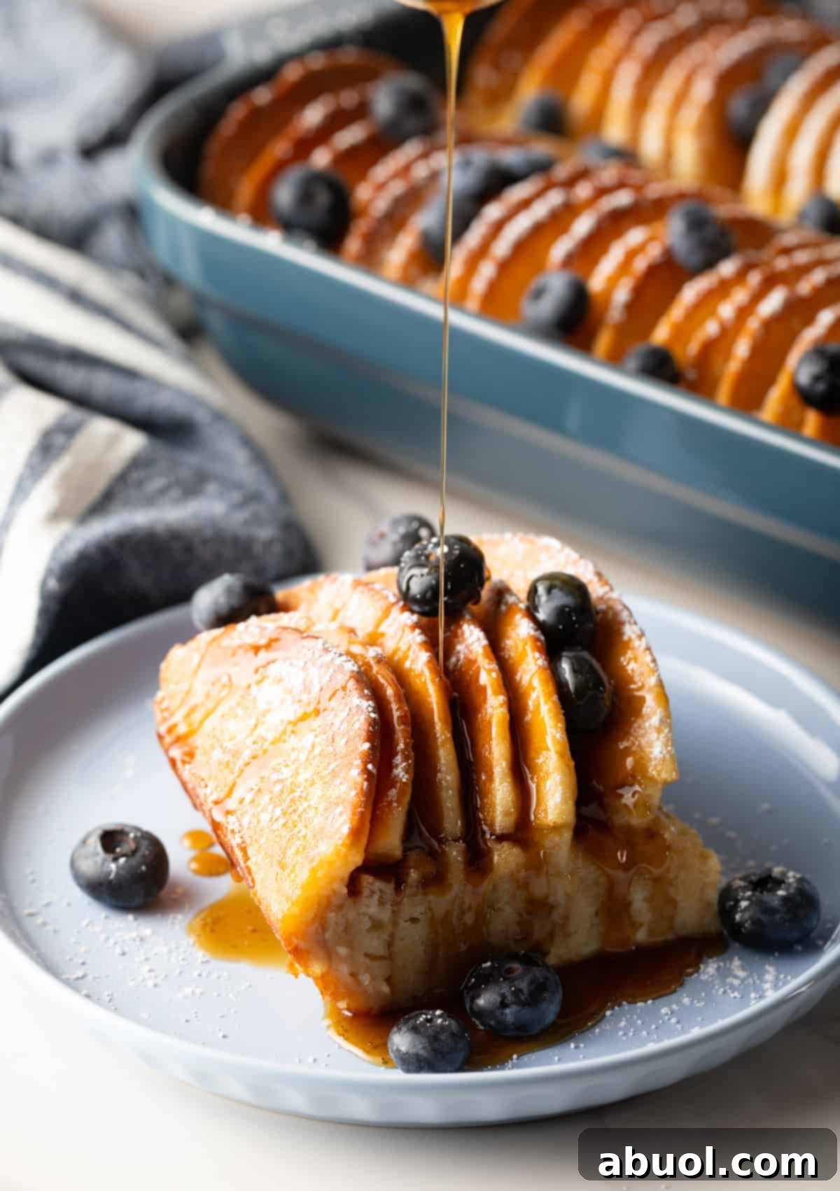 A slice of pancake casserole on a plate topped with blueberries and a drizzle of syrup.