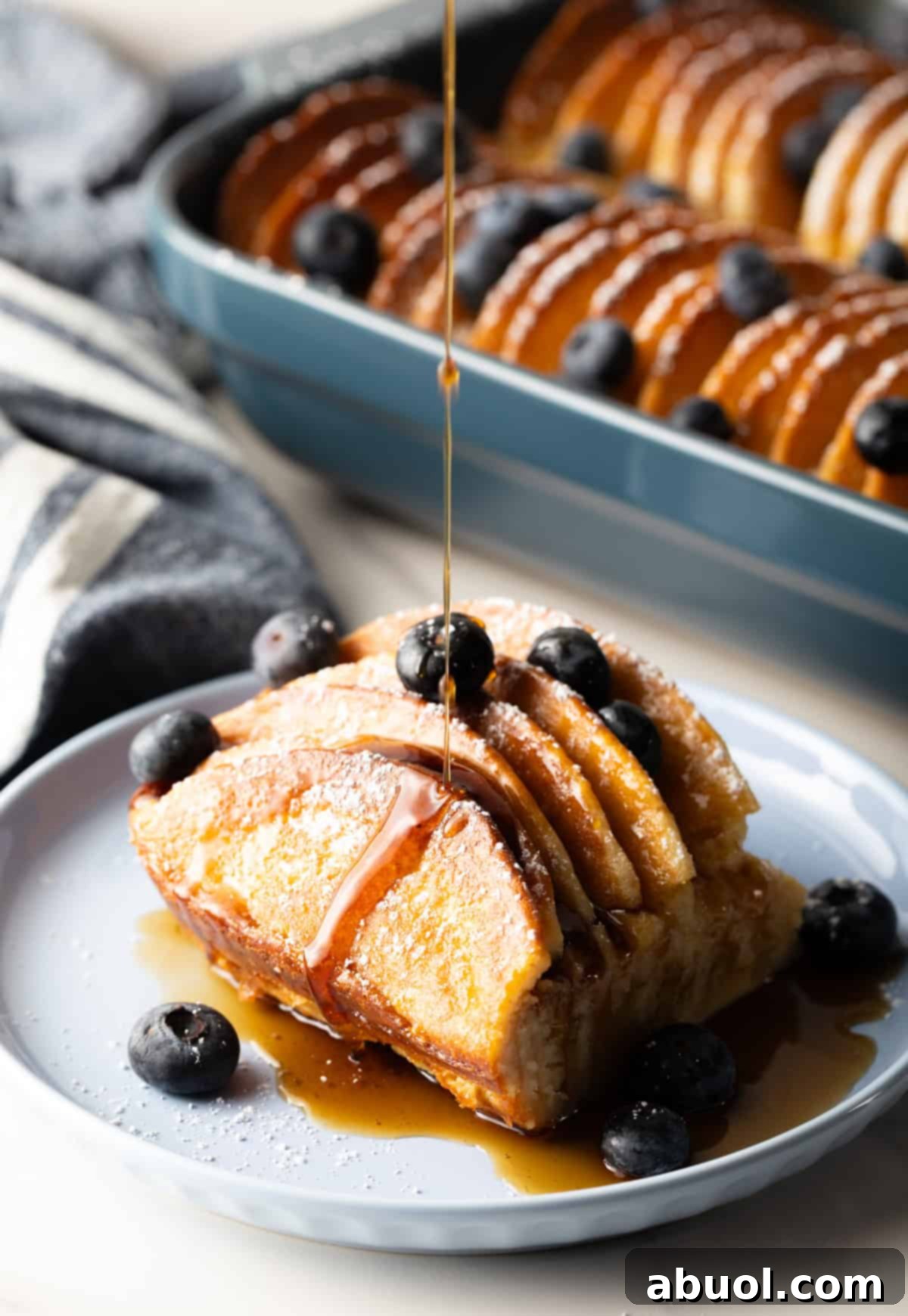 A slice of pancake casserole on a plate topped with blueberries and a drizzle of syrup.