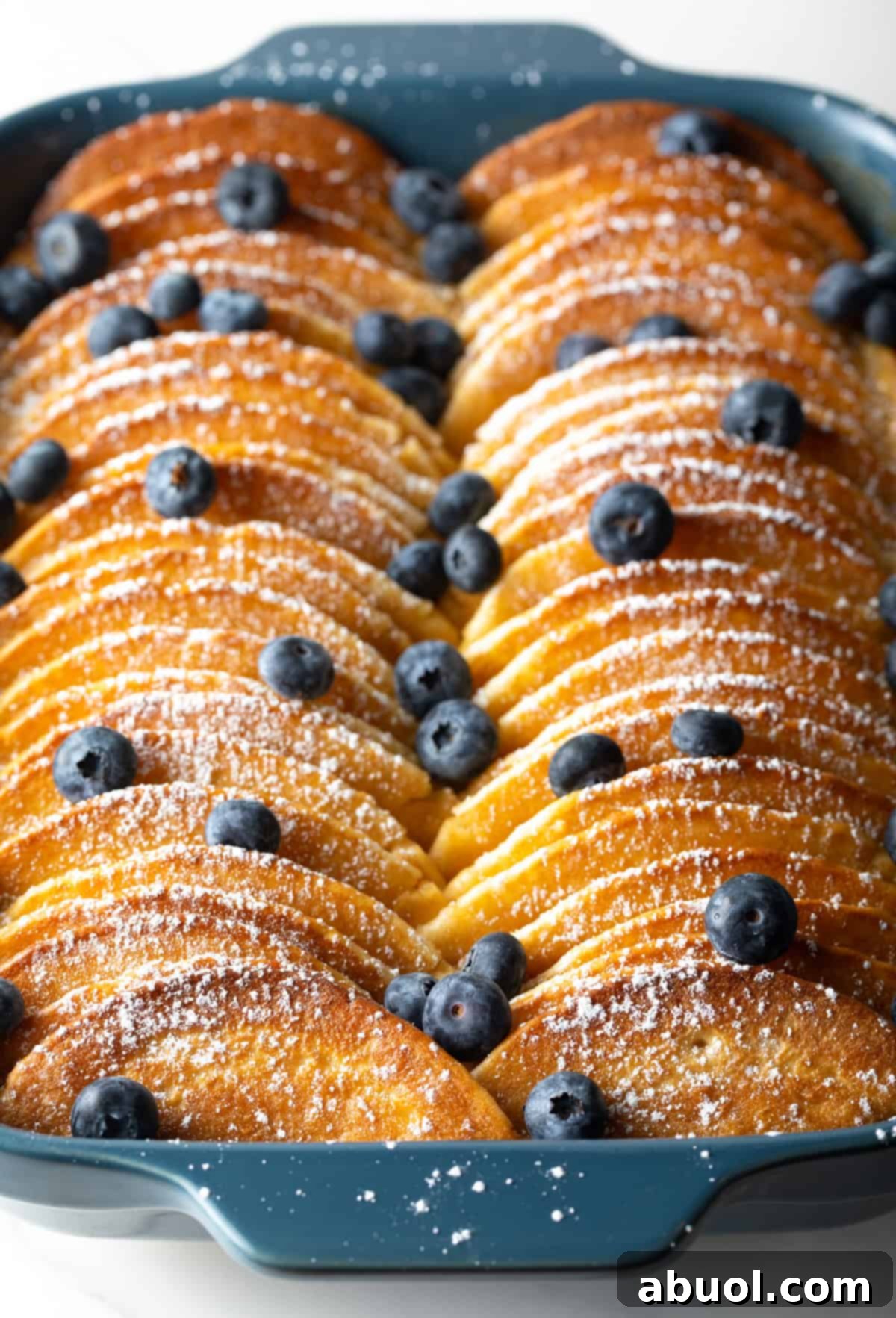 Blueberry-topped pancakes lined up in a blue casserole dish for a make-ahead pancake casserole recipe.