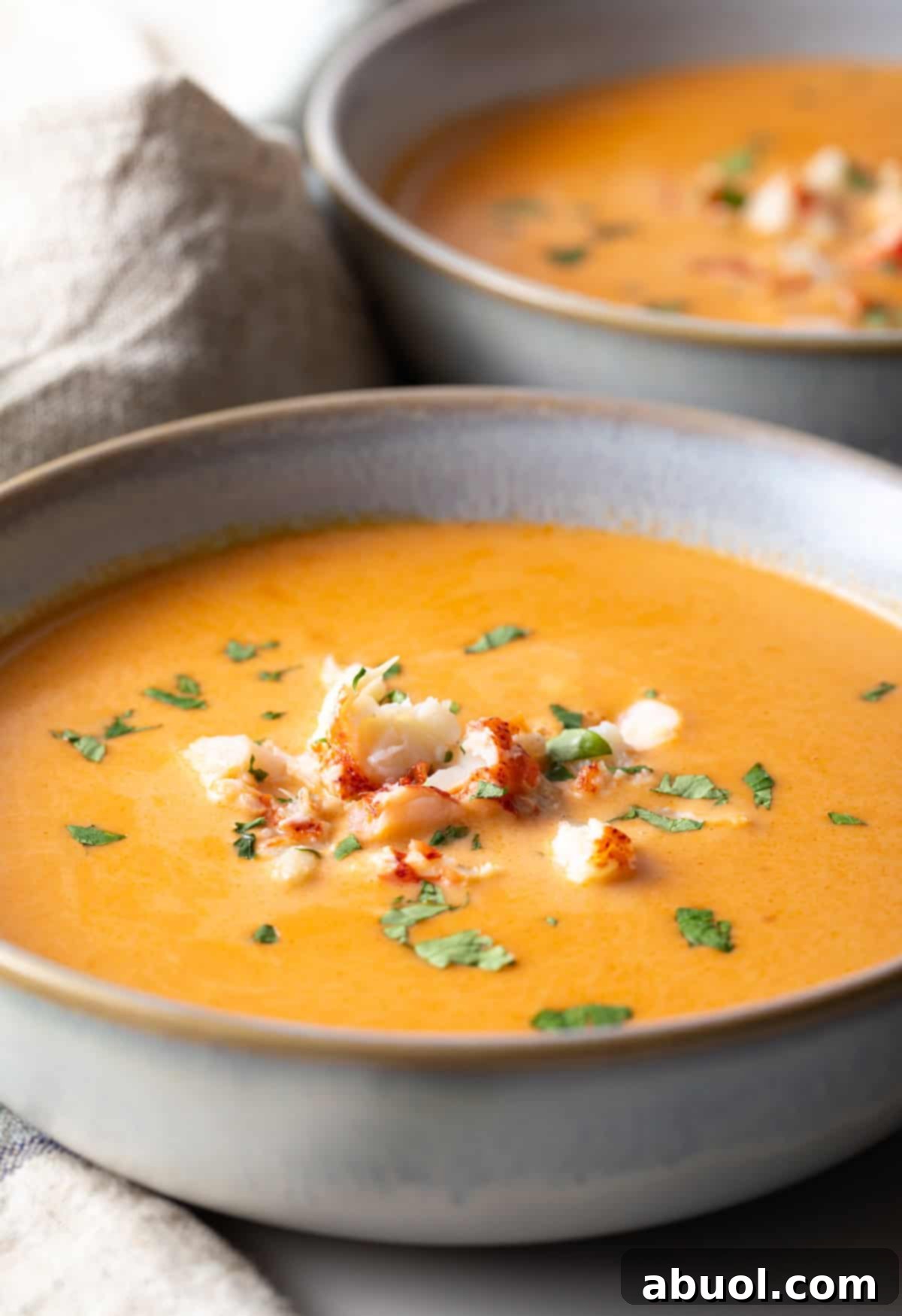 A bowl of creamy lobster bisque soup topped with lobster chunks and parsley.