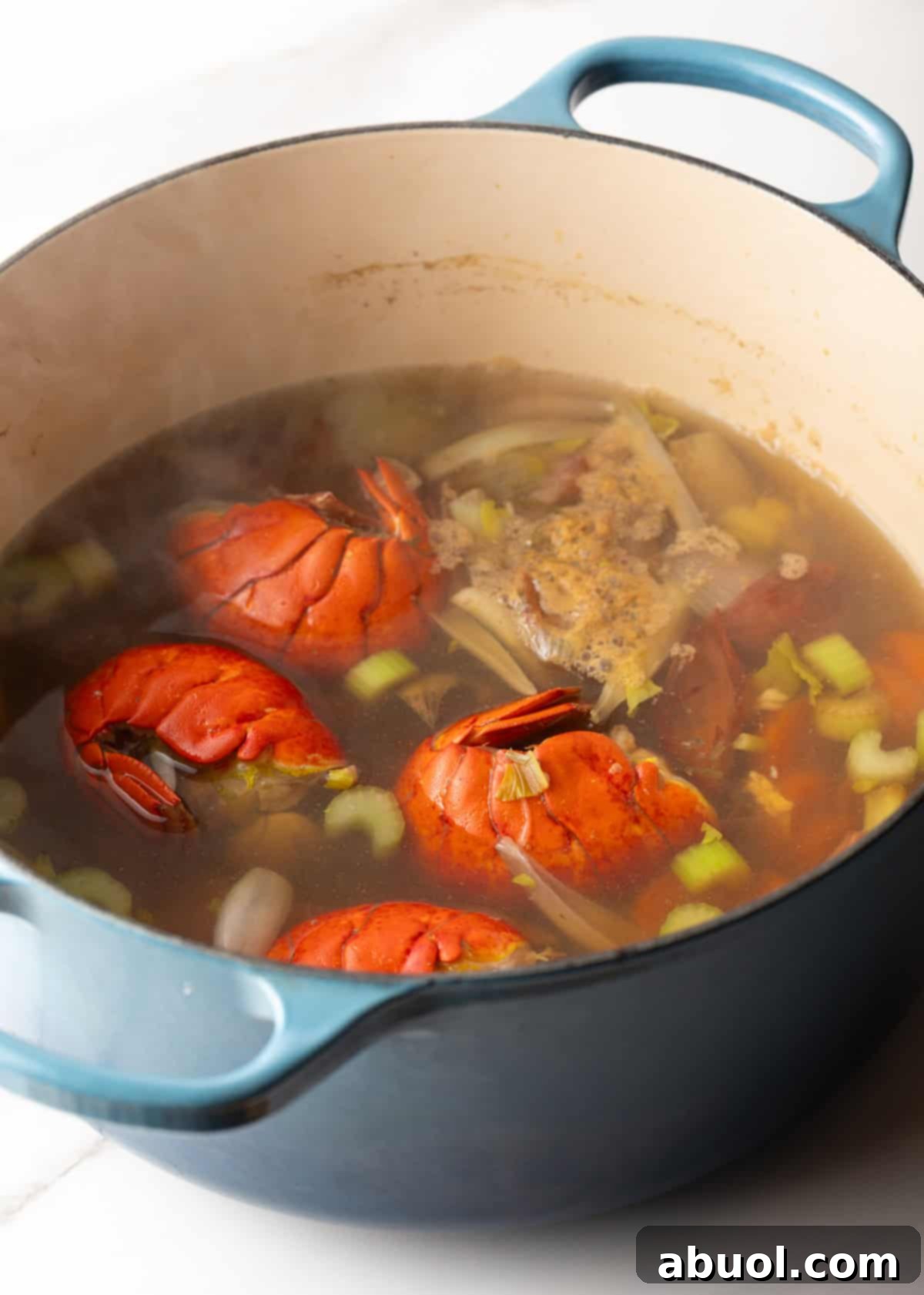 A pot simmering with seafood stock, lobster, and veggies.