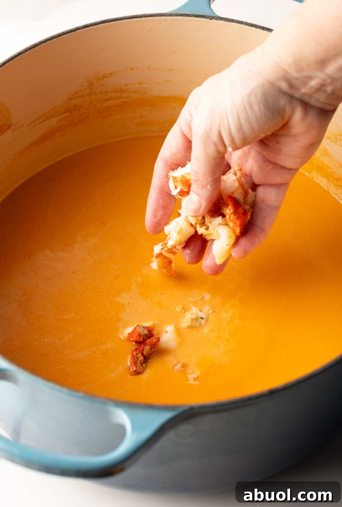 Lobster chunks are being added to a pot full of creamy lobster bisque recipe.