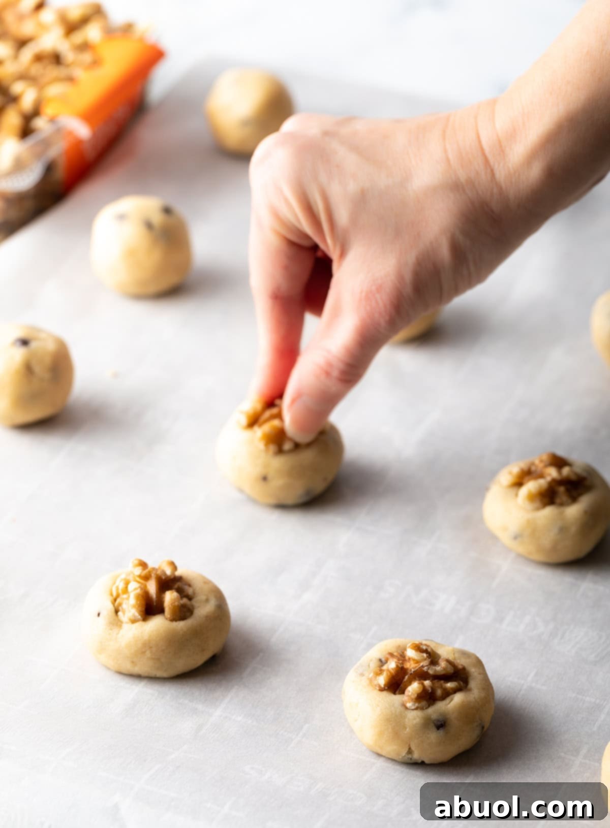 Halved walnuts being pressed into cookie dough.