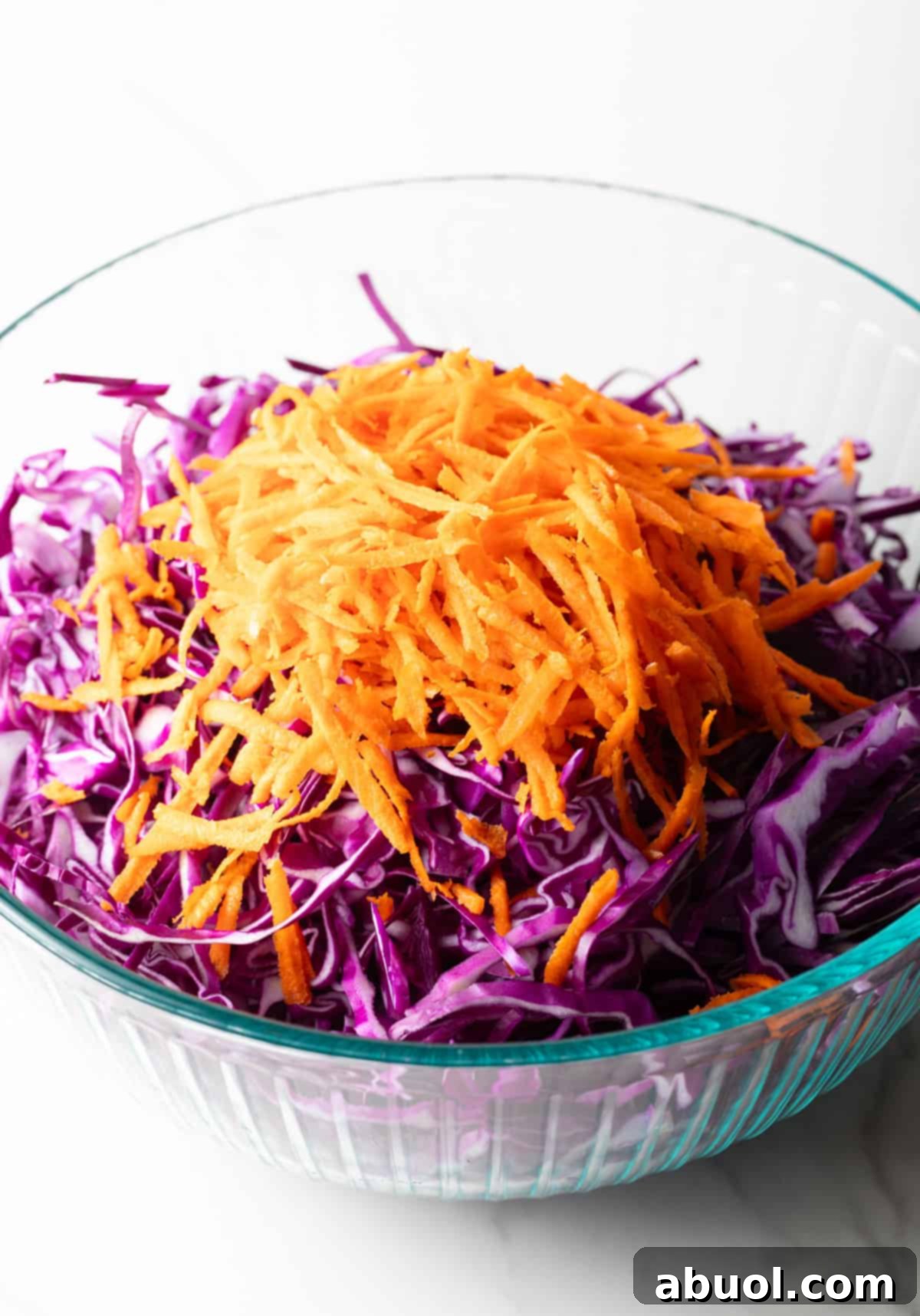 A glass bowl filled with shredded red cabbage, red onion, and carrots, ready to be dressed.