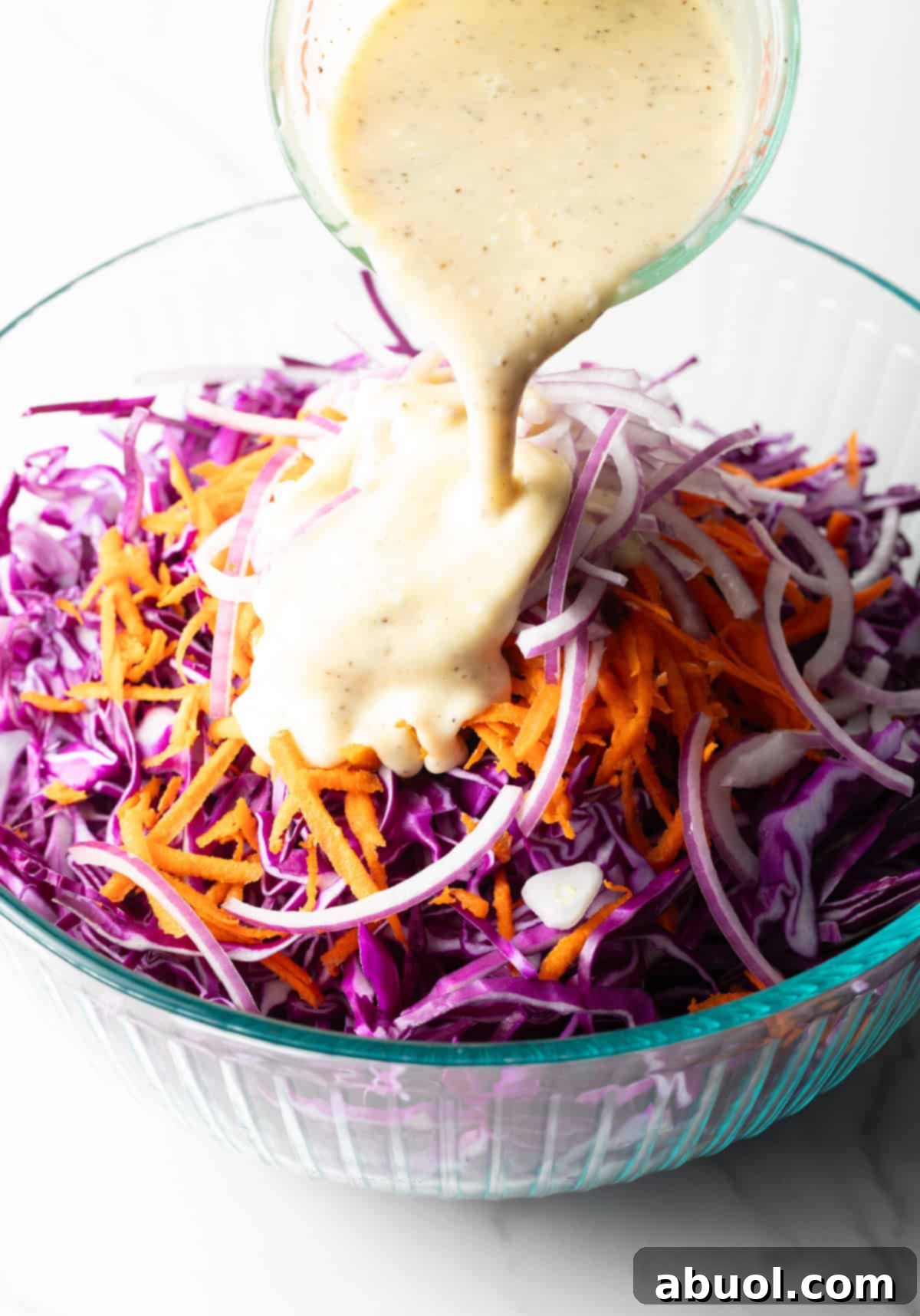 Pouring the creamy mayonnaise dressing over the colorful red cabbage slaw.