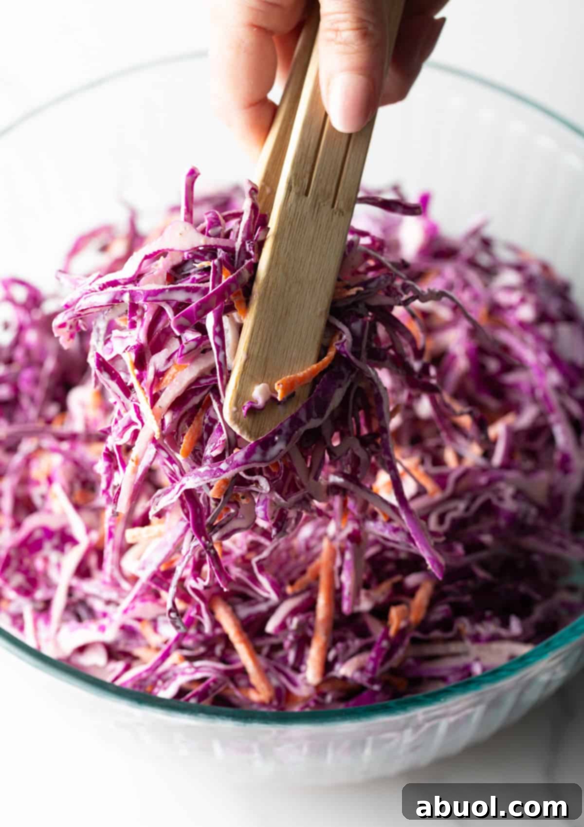 Using wooden tongs to gently toss the red cabbage slaw, ensuring the dressing is evenly distributed.