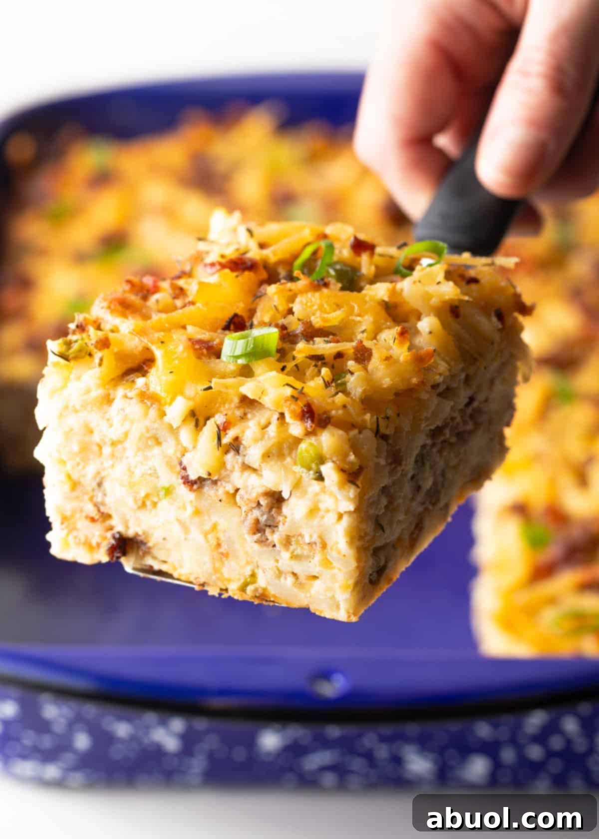 A tempting slice of hashbrown breakfast casserole being lifted from a blue baking dish with a metal spatula.