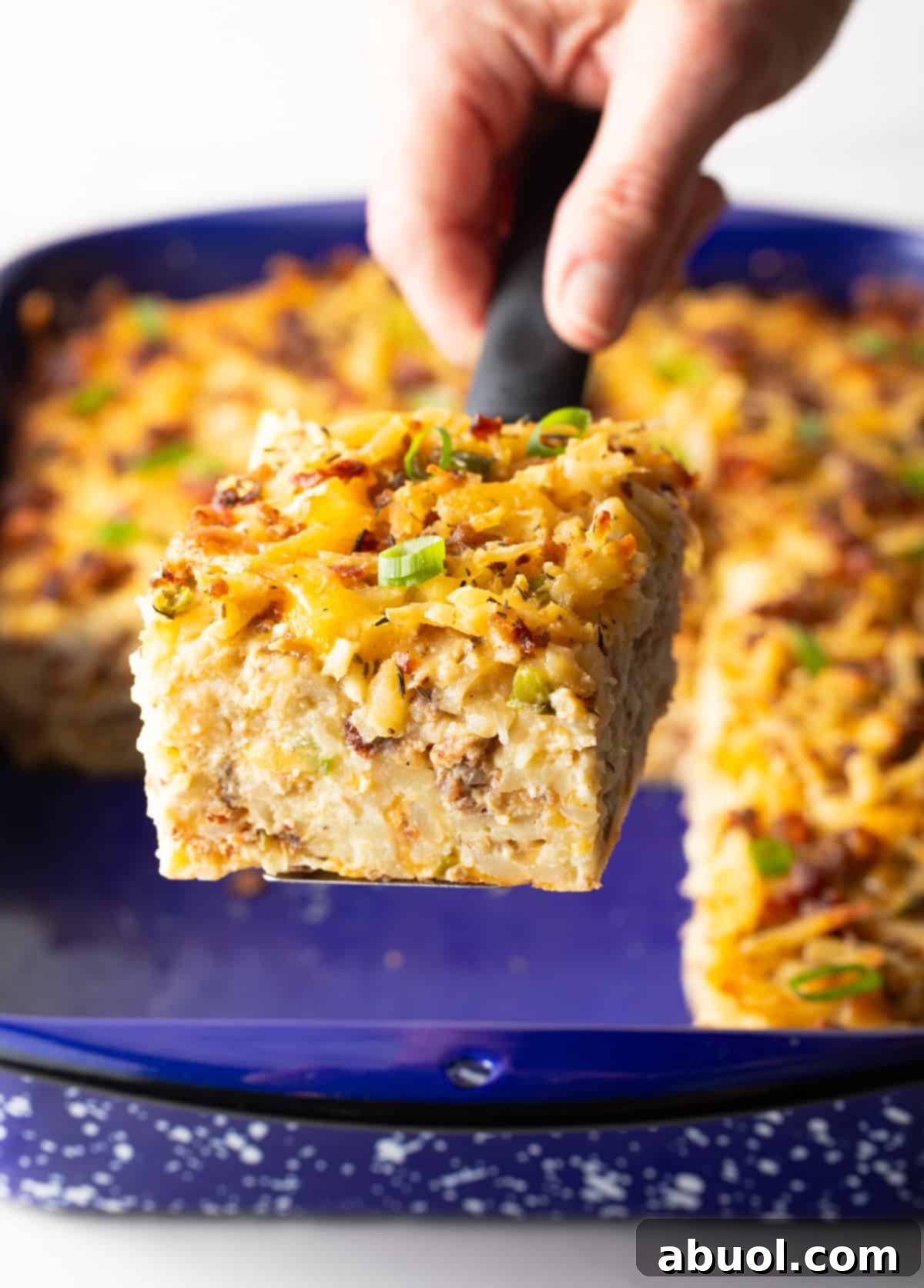 A hand proudly presenting a square of hash brown breakfast casserole towards the camera.