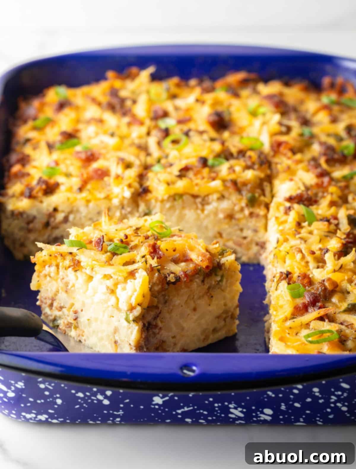 A delectable hash brown breakfast casserole in a vibrant blue baking dish, with a slice elegantly presented by a metal spatula.