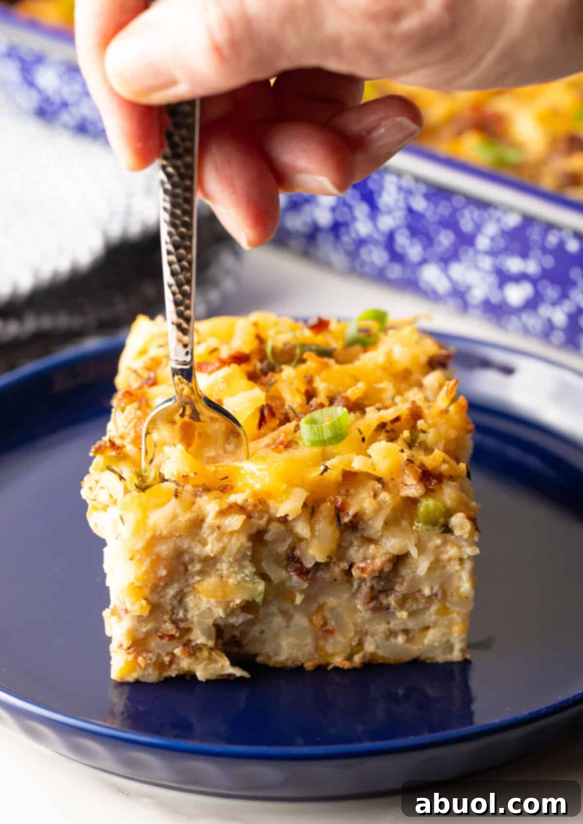 A delightful slice of hash brown breakfast casserole on a blue plate, with a fork poised to take a delicious bite.