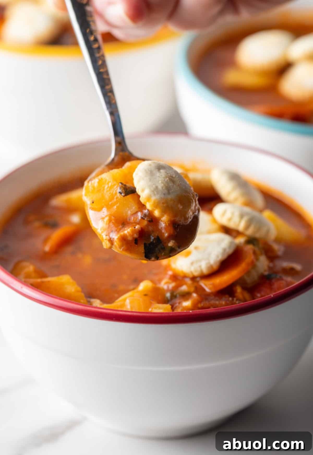 Close-up of Manhattan clam chowder on a spoon with oyster crackers.