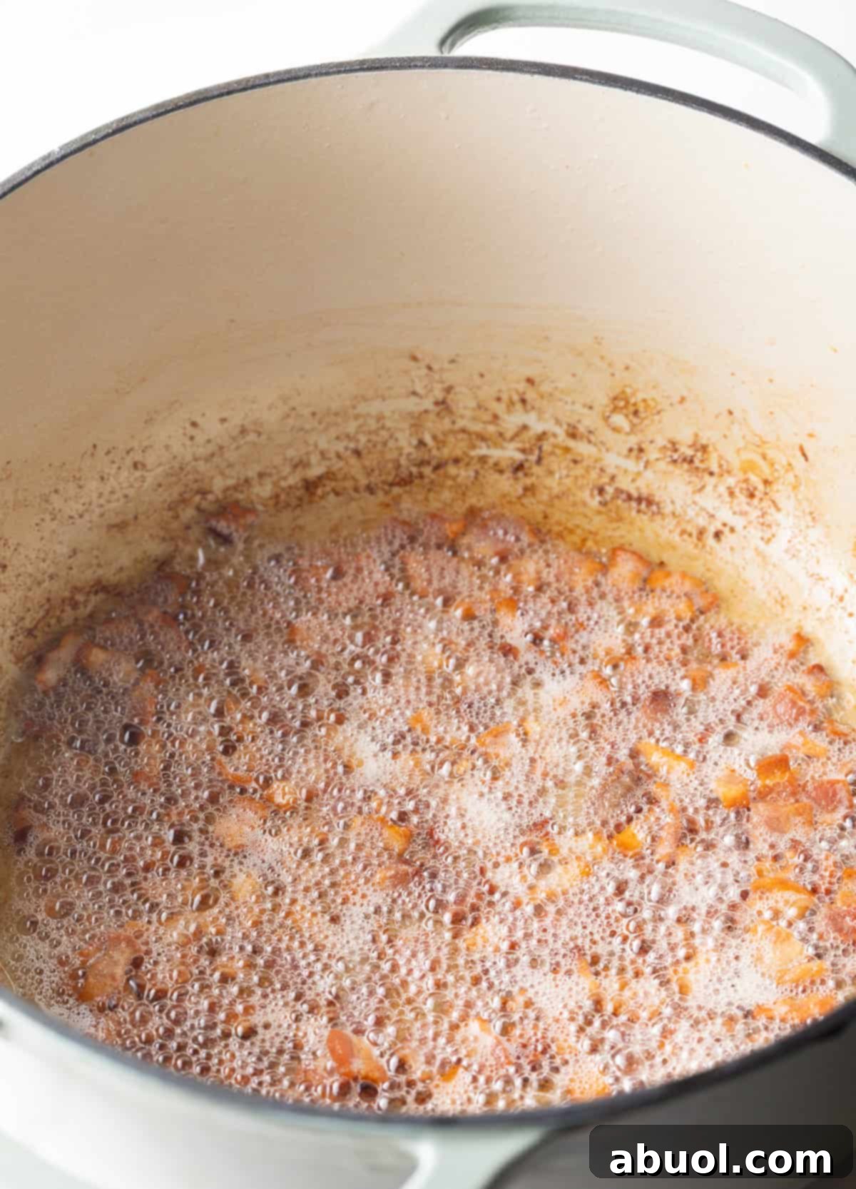 Bacon being sautéed in a metal pot.