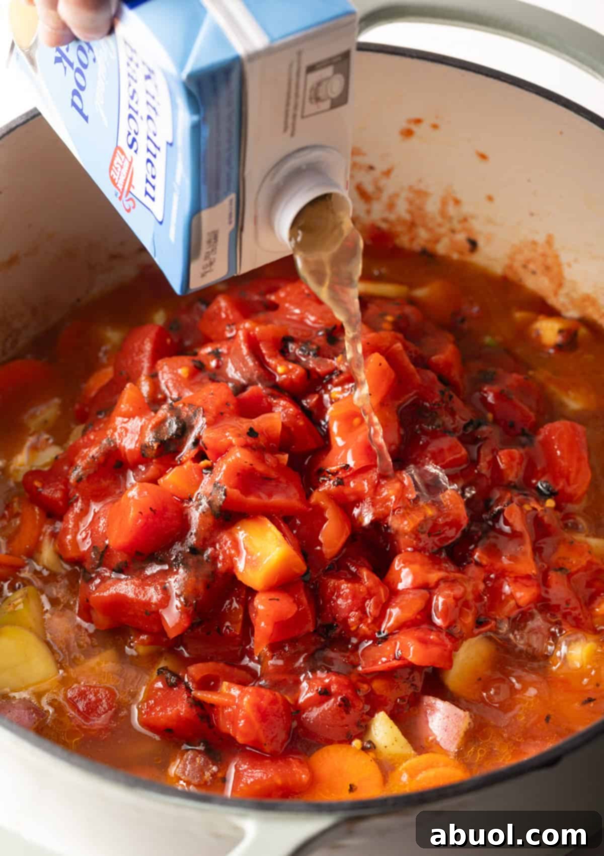 Seafood stock being poured into the pot with vegetables and tomatoes.