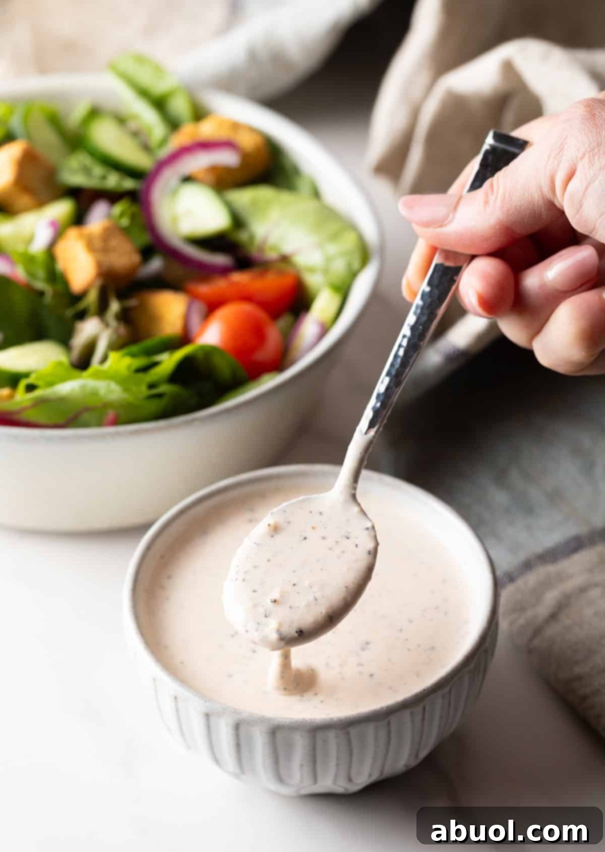 A spoonful of Parmesan Peppercorn Dressing held over a bowl, next to a salad