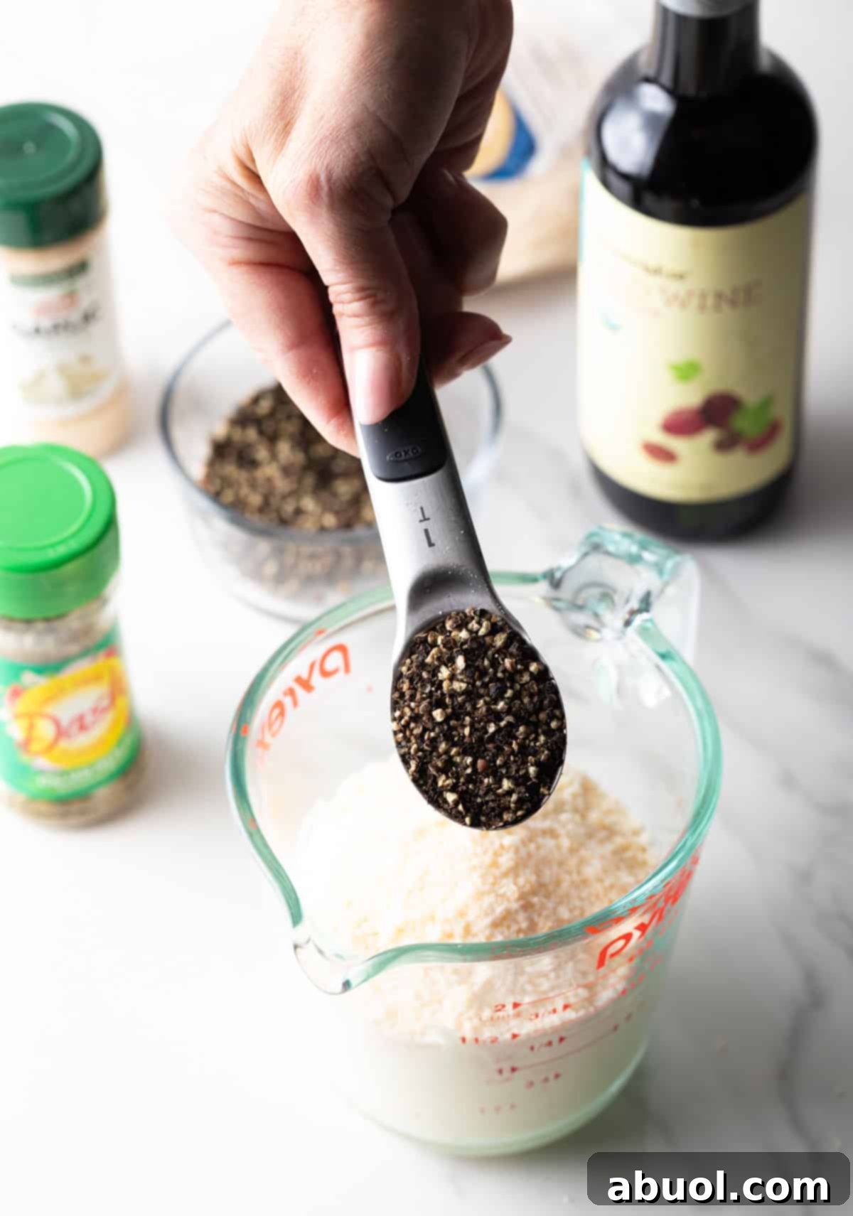 Ground peppercorns being added to a mixture of parmesan cheese and mayonnaise