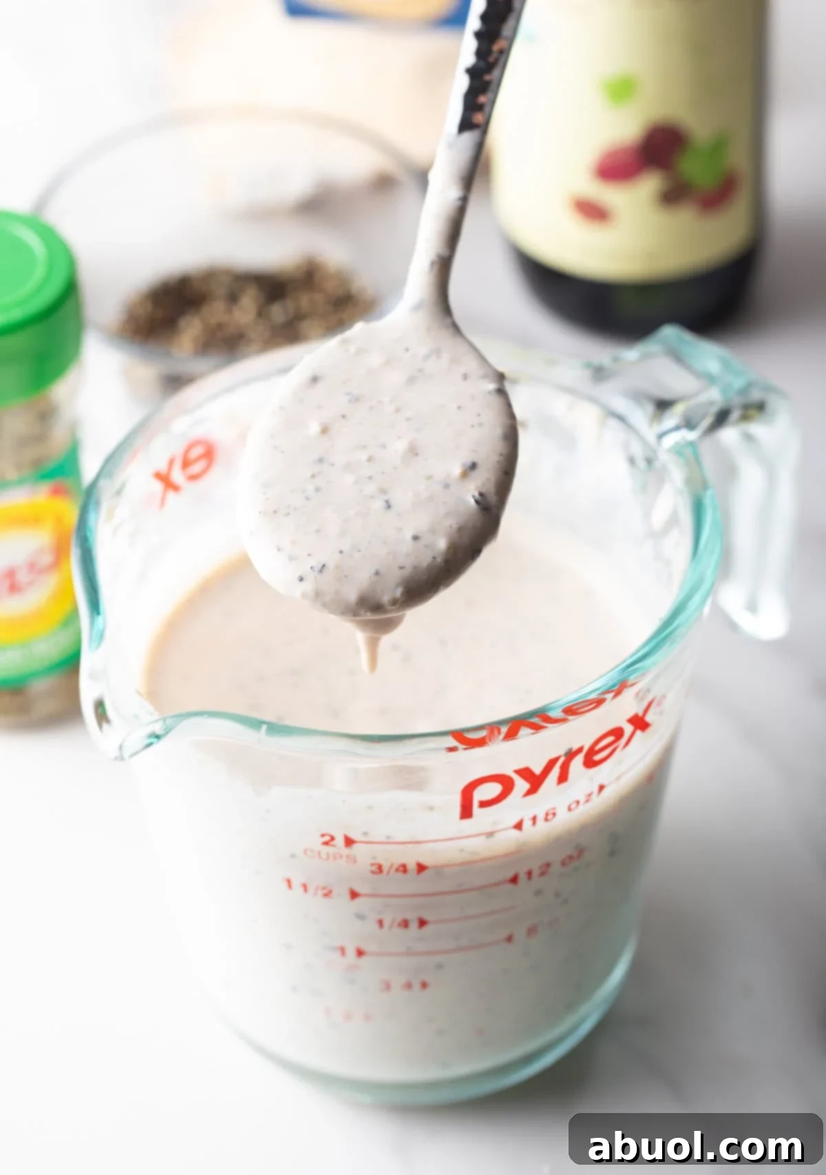 Fully mixed Parmesan Peppercorn Dressing on a spoon over a glass measuring cup