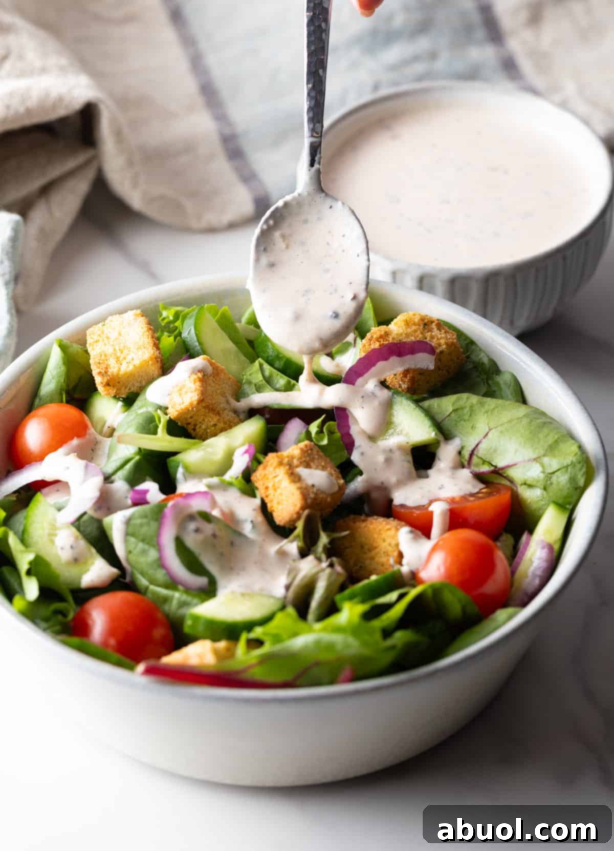 Parmesan Peppercorn Dressing being ladled over a fresh garden salad