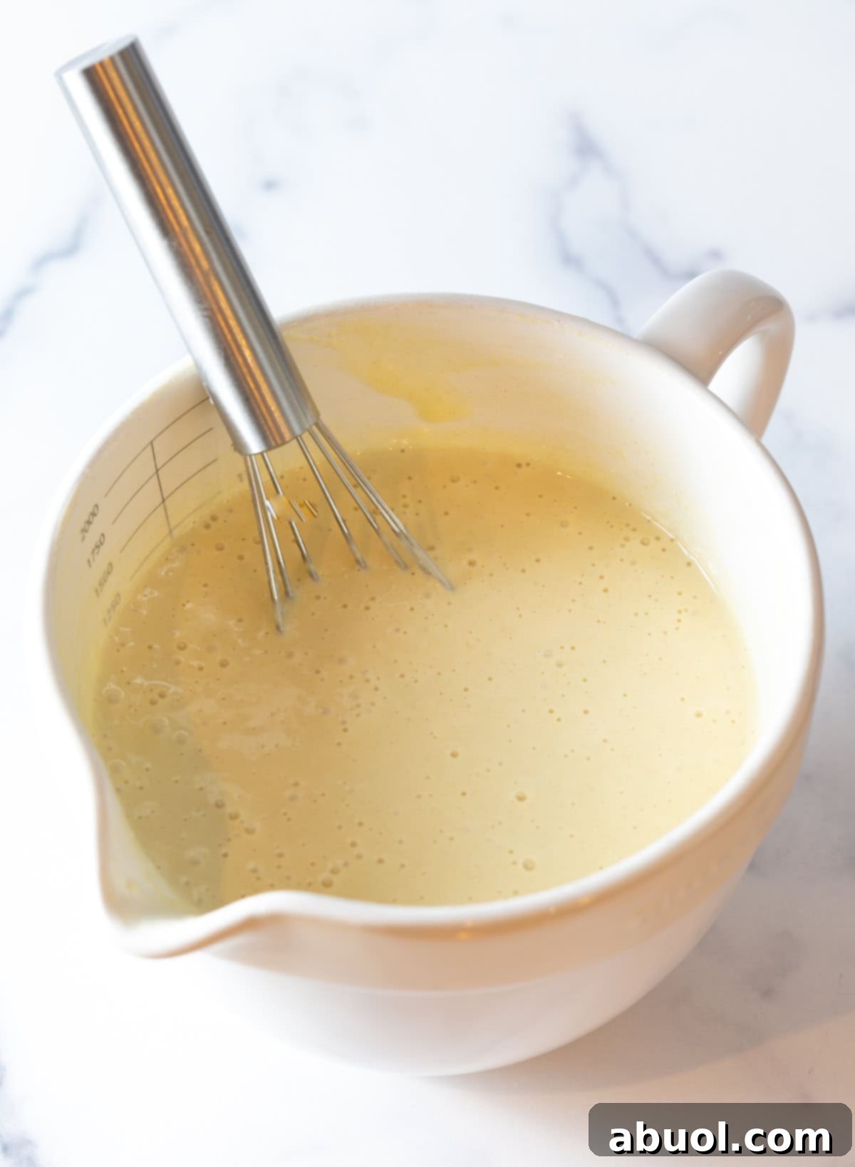 Homemade funnel cake batter being whisked in a white mixing bowl.