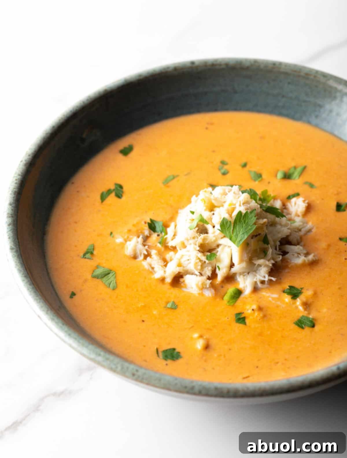 A black bowl filled with creamy crab bisque soup with crab meat and parsley on top, garnished elegantly.