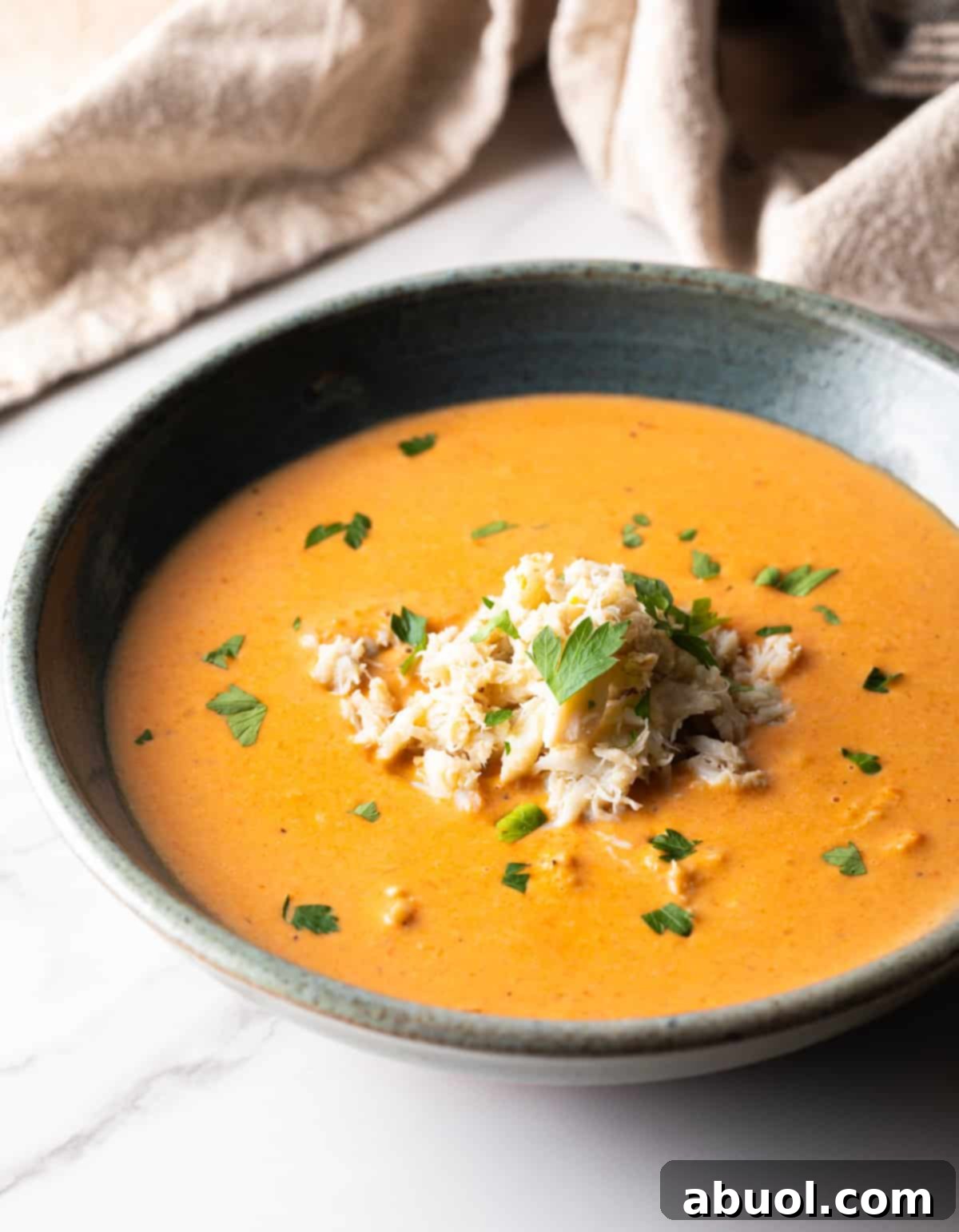 A grey bowl filled with a creamy crab bisque soup recipe, garnished with vibrant crab meat and fresh parsley on top.