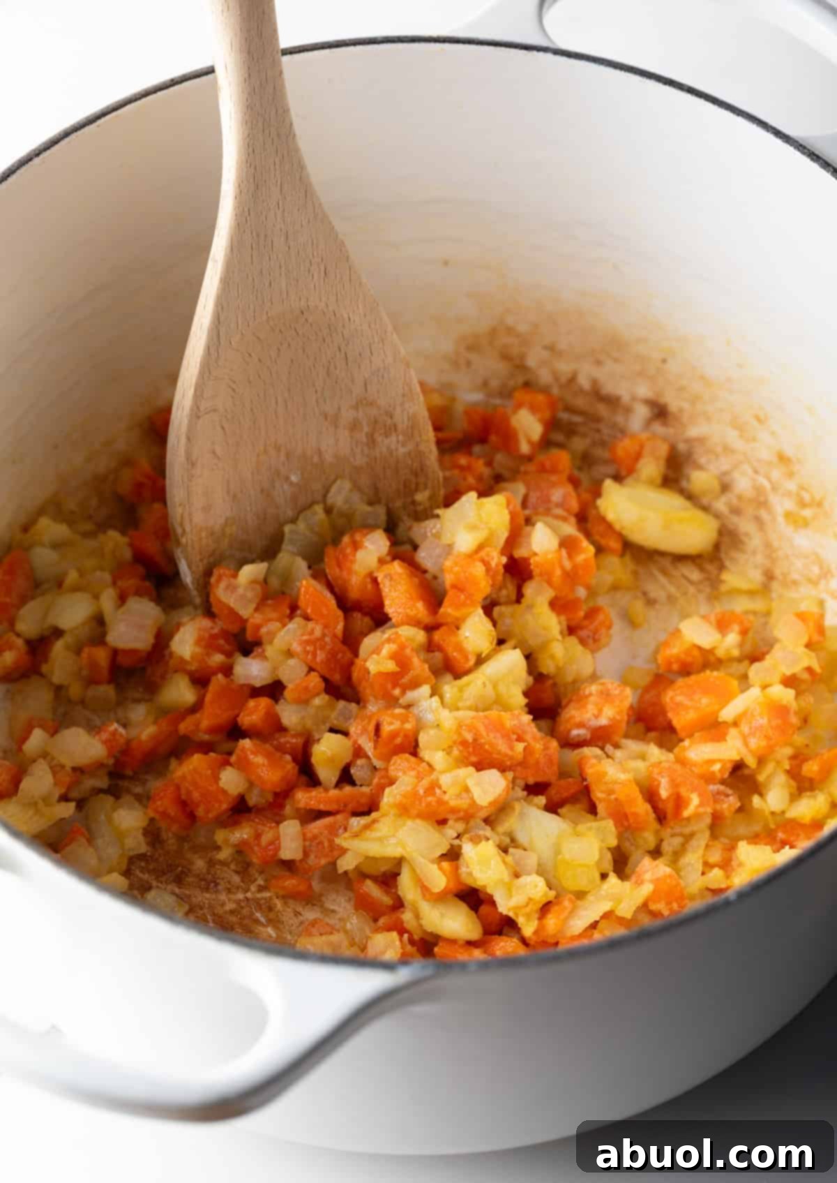 Flour is being stirred into the sautéed veggie mixture in a large pot, forming a roux.
