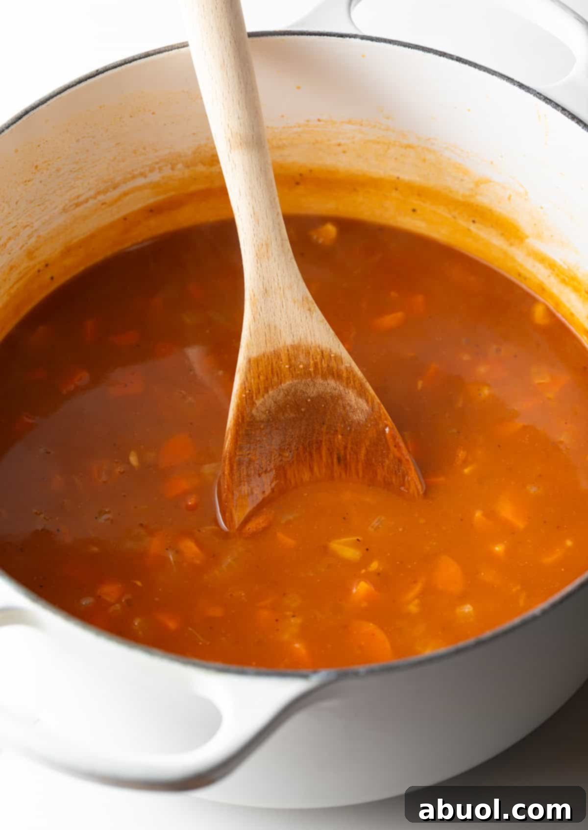 A rich crab bisque soup base is being simmered and stirred in a white pot, building deep flavors.