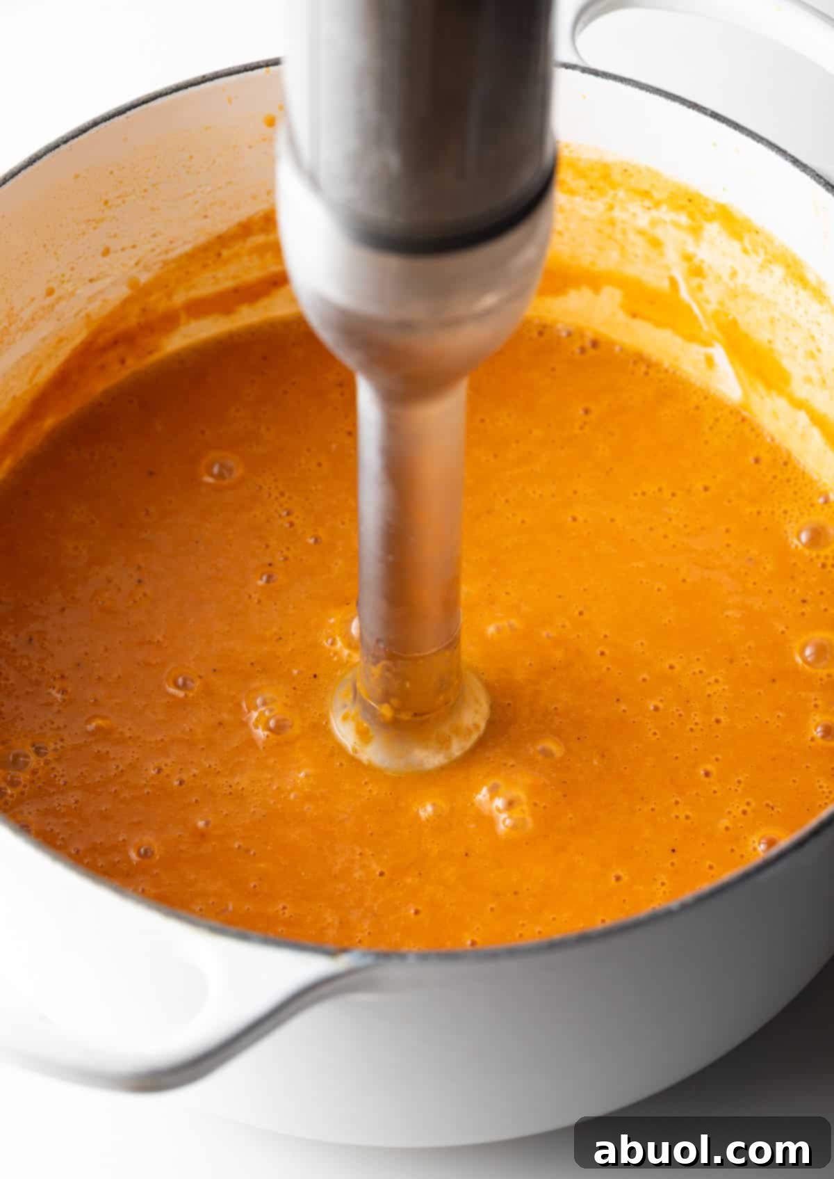 An immersion blender smoothly blending a rich crab bisque soup base in a pot.