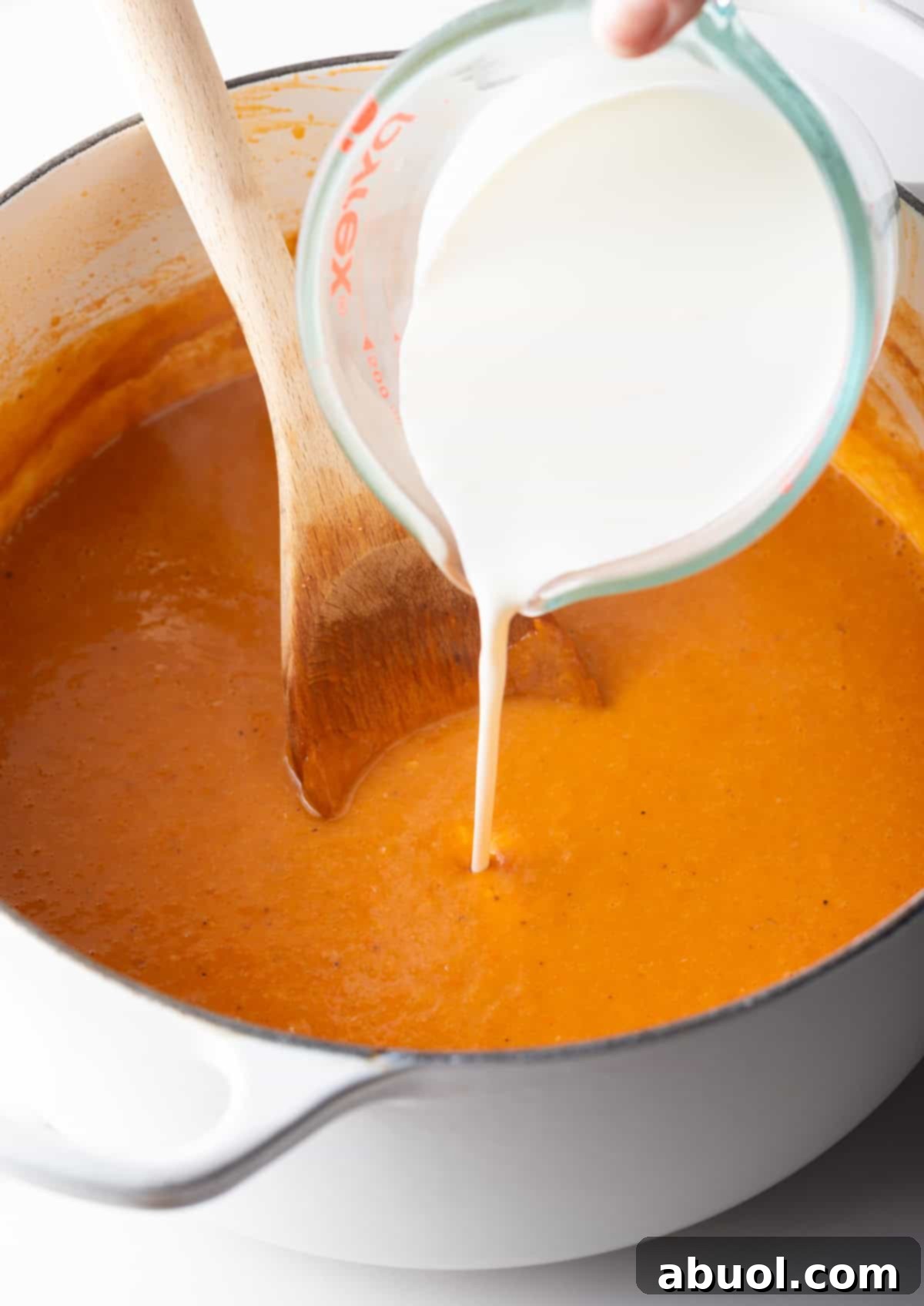 Heavy cream being poured into a crab bisque recipe soup base, creating a rich and velvety texture.