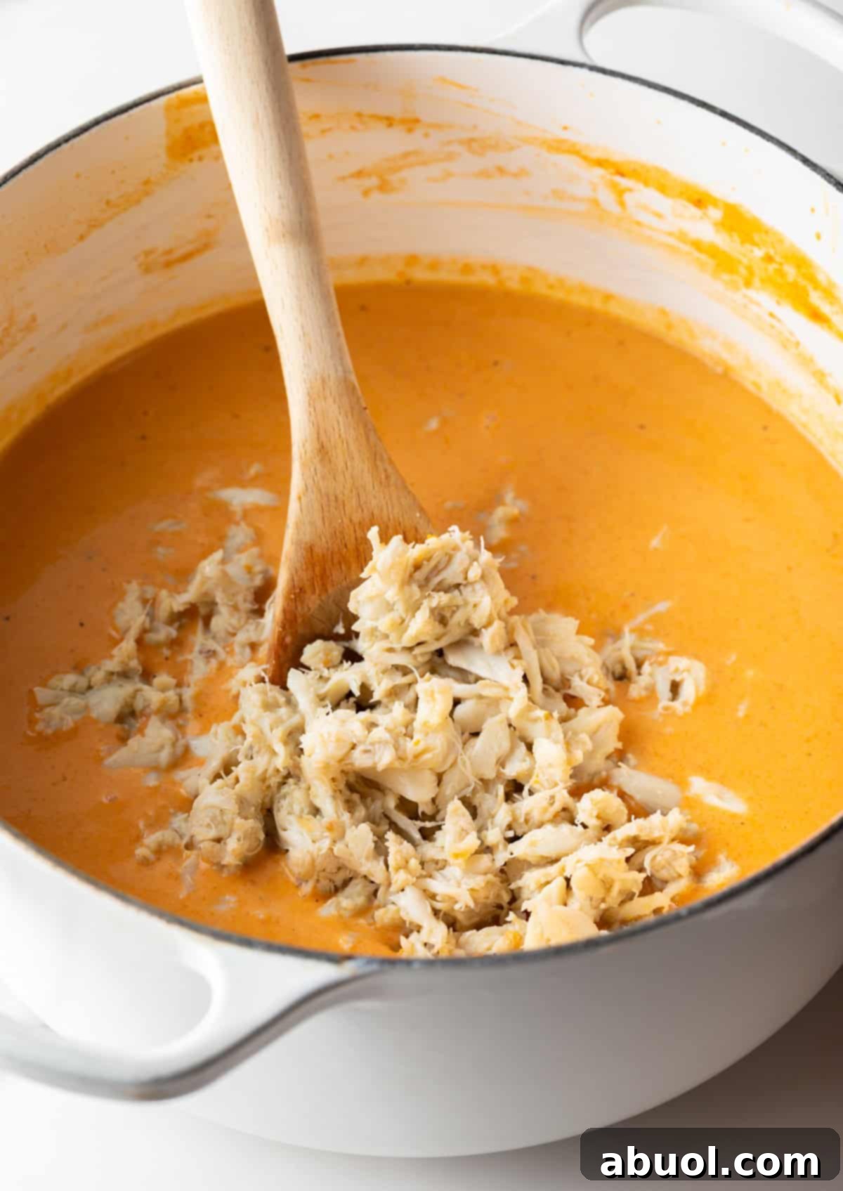 Lump crab meat being gently added to a creamy crab bisque soup recipe in a large pot.