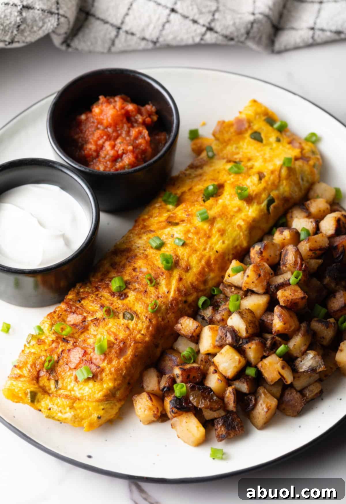 A Denver omelet between home fries and two black ramekins filled with sauce, on a white plate.