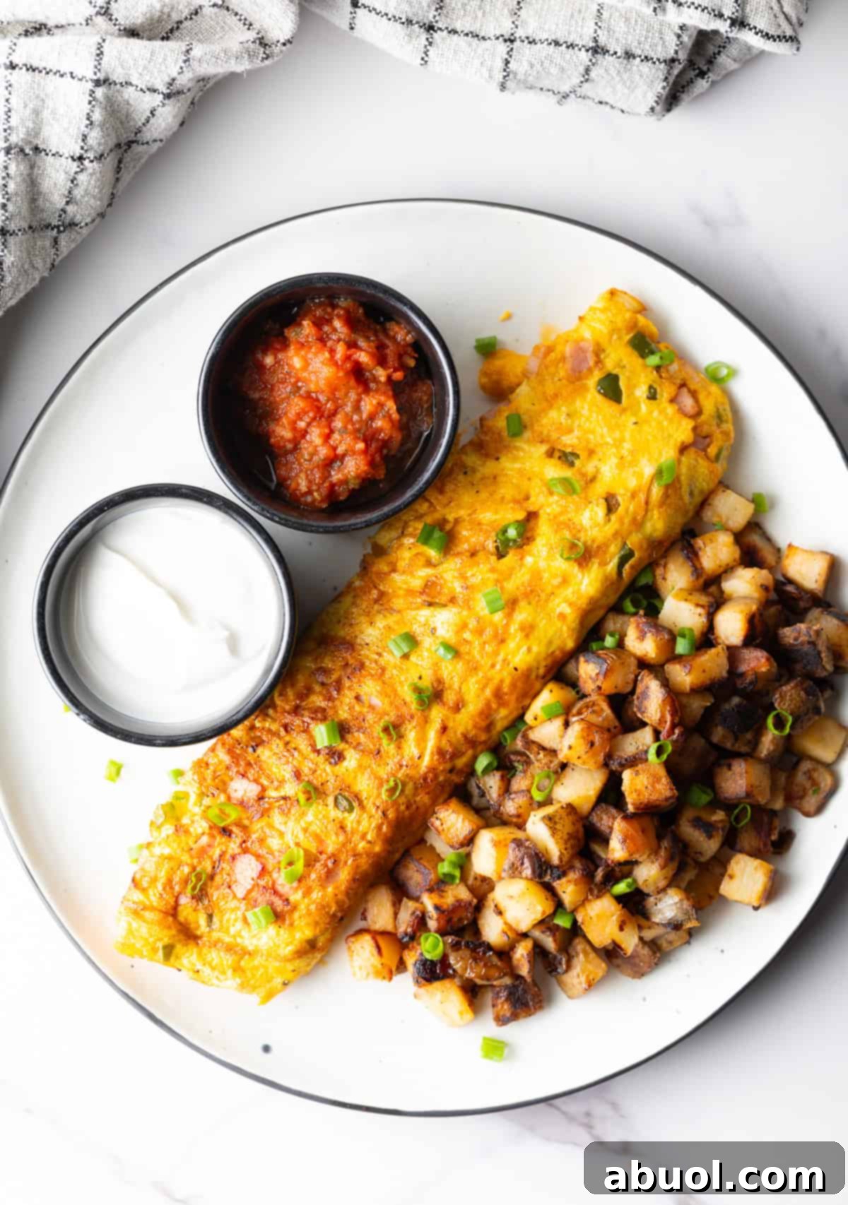 An overhead view of a Denver omelet, breakfast potatoes, and ramekins of sauce, on a white plate.