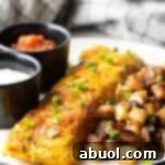 A Denver omelette between breakfast potatoes and two black ramekins filled with sauce, on a white plate.