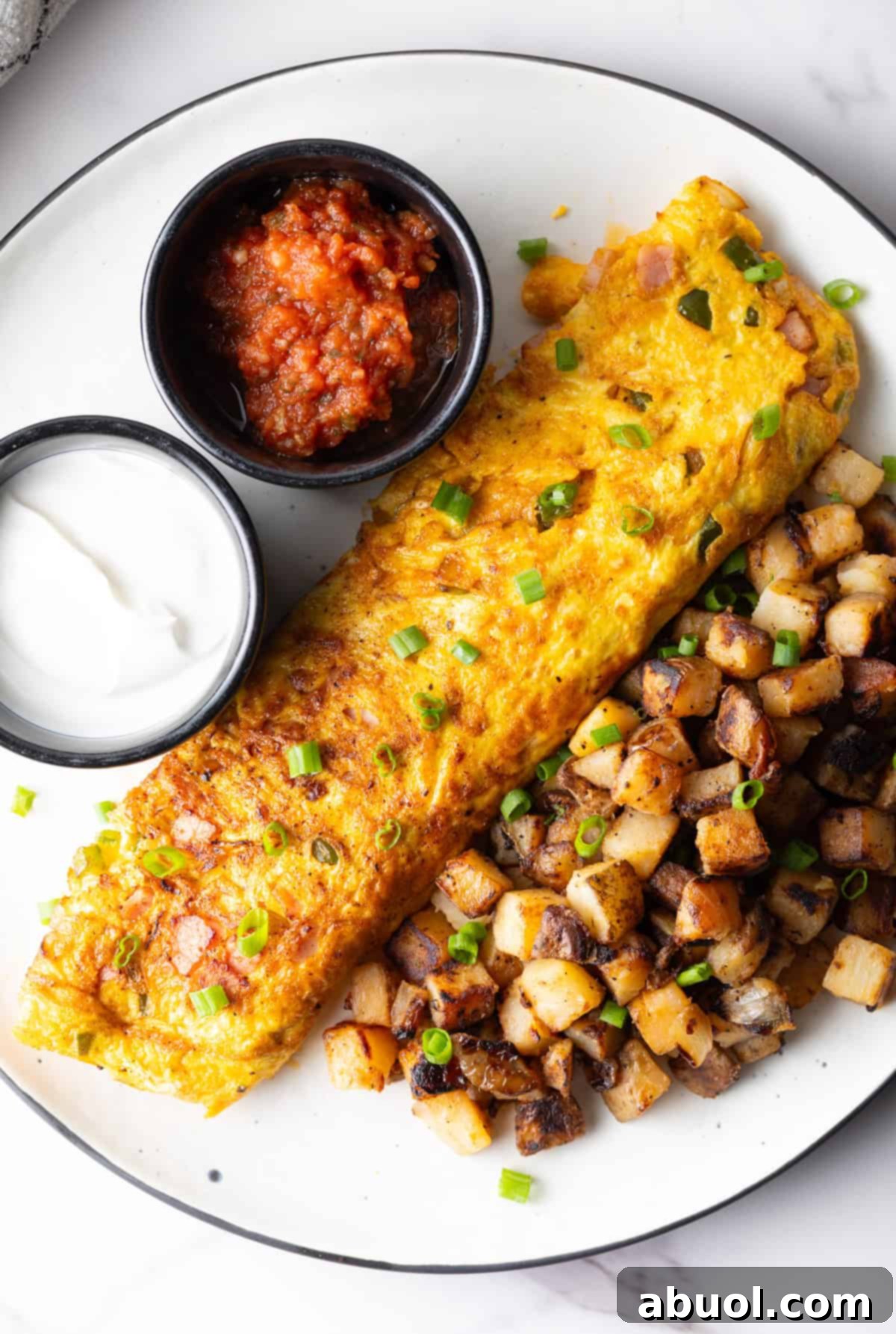 An overhead view of a Denver omelet, breakfast potatoes, and ramekins of sauce, on a white plate.