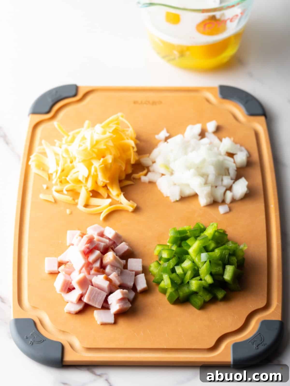 Diced onion, peppers, ham, and shredded cheese in four piles on a wooden cutting board.