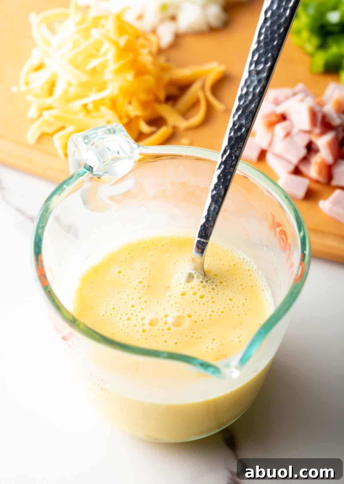 An egg and cream mixture is being mixed in a glass measuring bowl.
