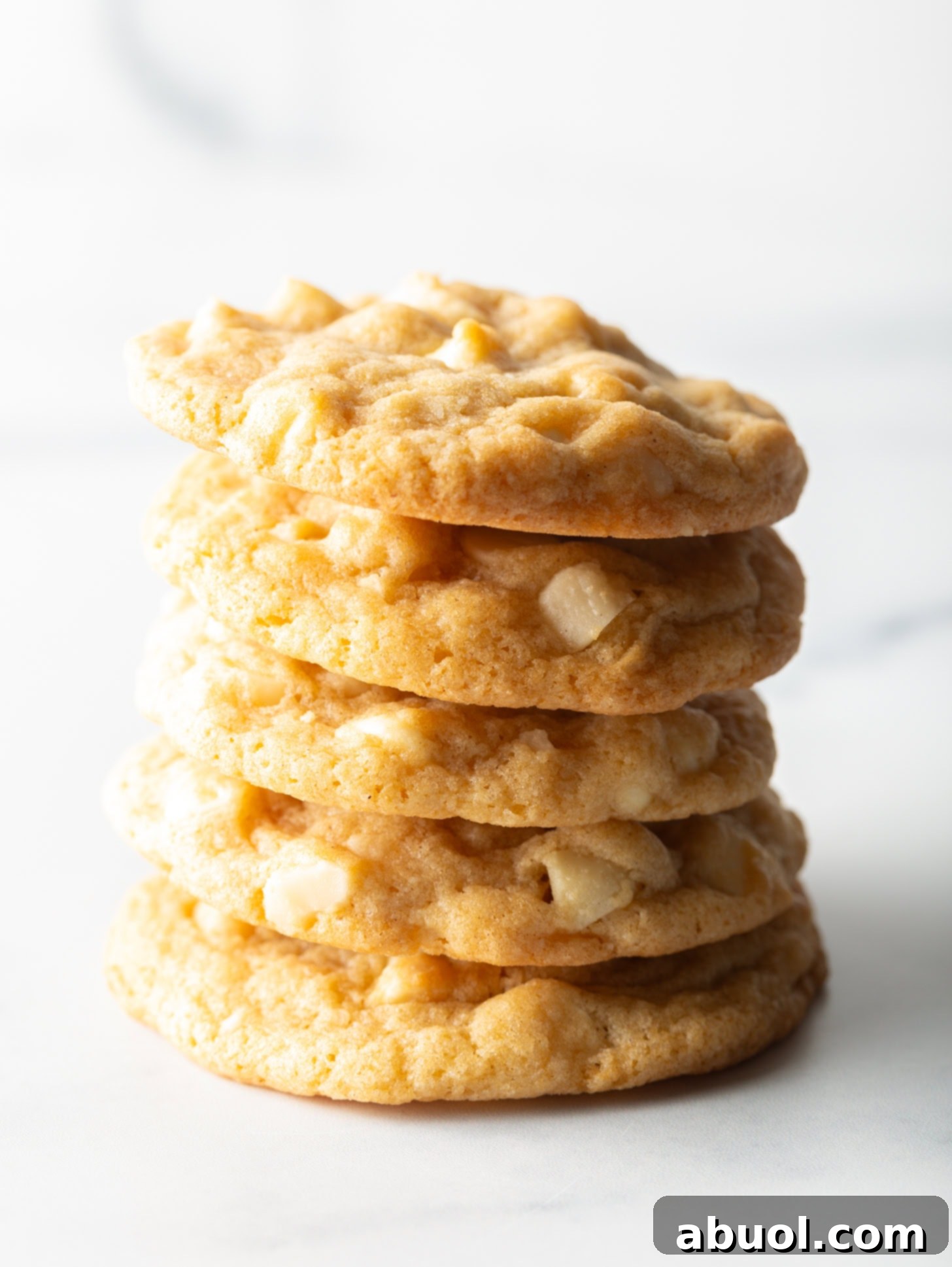 A beautifully arranged stack of five golden white chocolate macadamia nut cookies, showcasing their rich texture and generous filling.