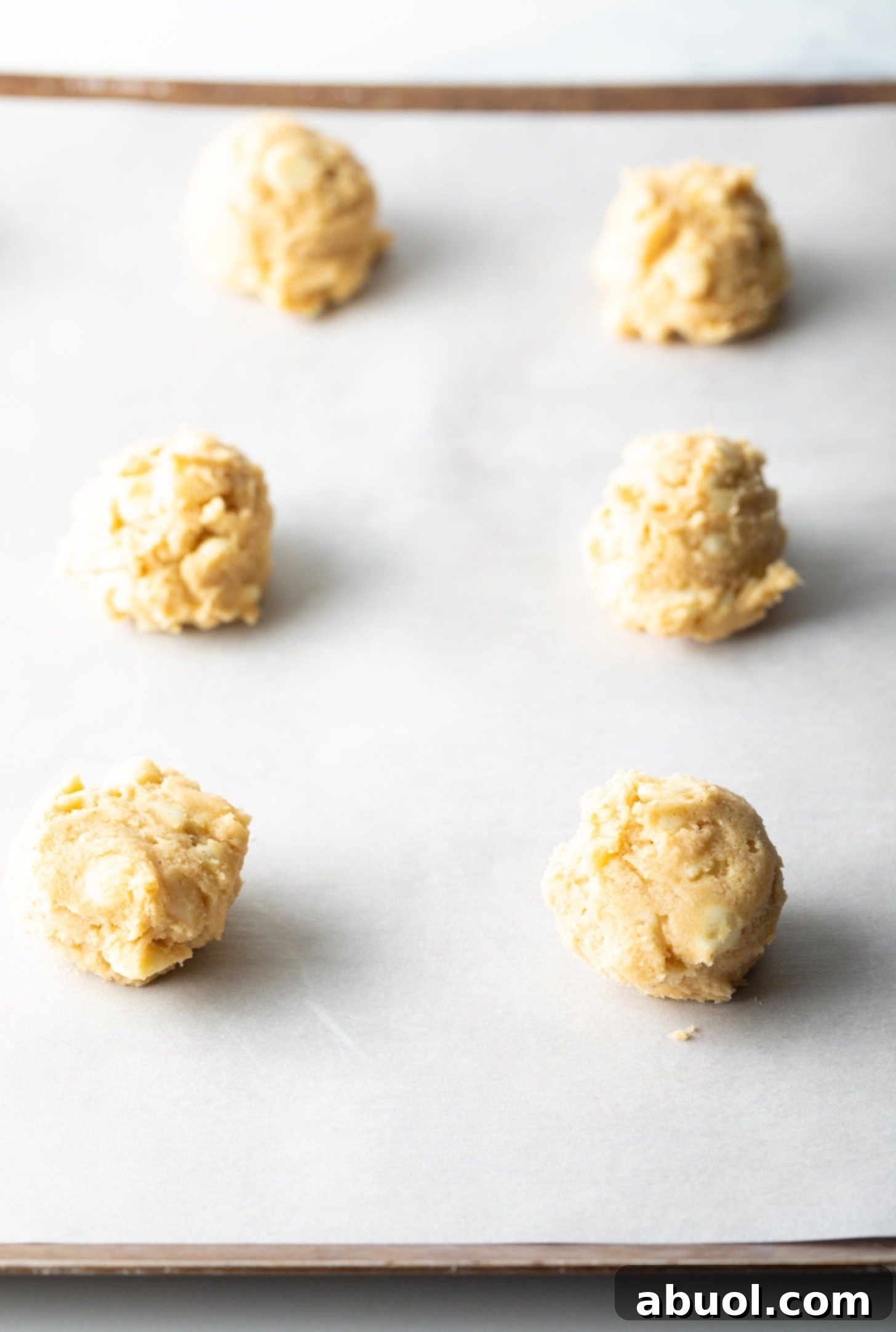 Six perfectly scooped balls of white chocolate macadamia nut cookie dough arranged on parchment paper, ready for baking.