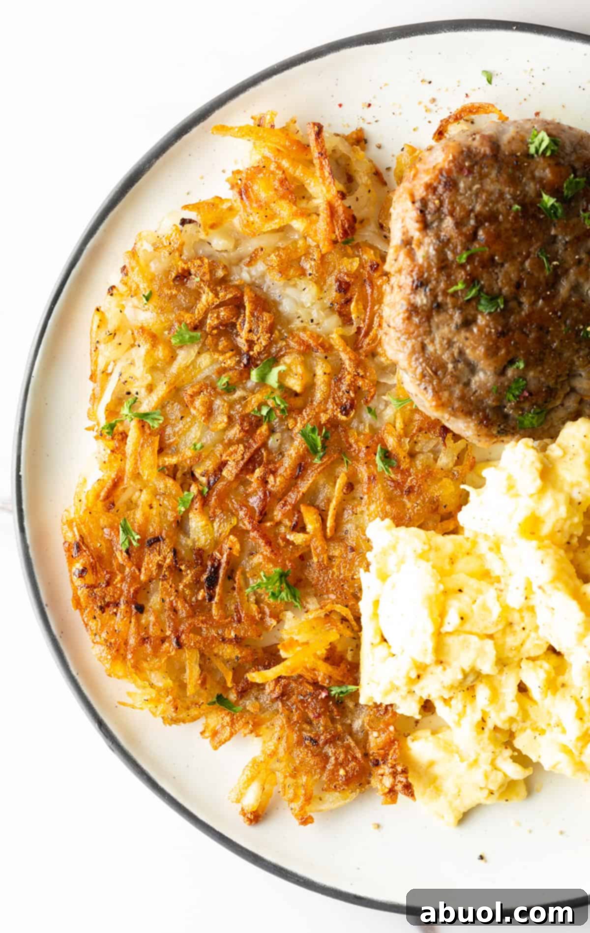 Crispy homemade hash browns, breakfast sausage, and scrambled eggs on a white plate.