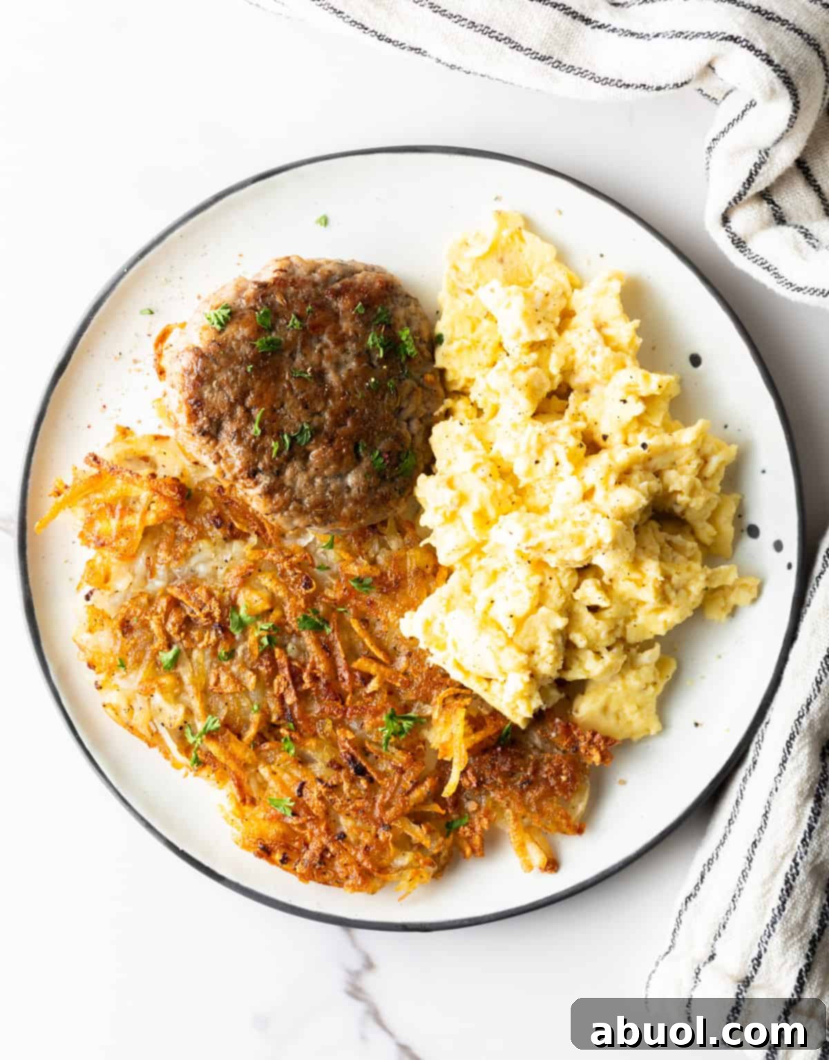 An overhead shot of a white plate filled with homemade hashbrown potatoes, breakfast sausage, and scrambled eggs.