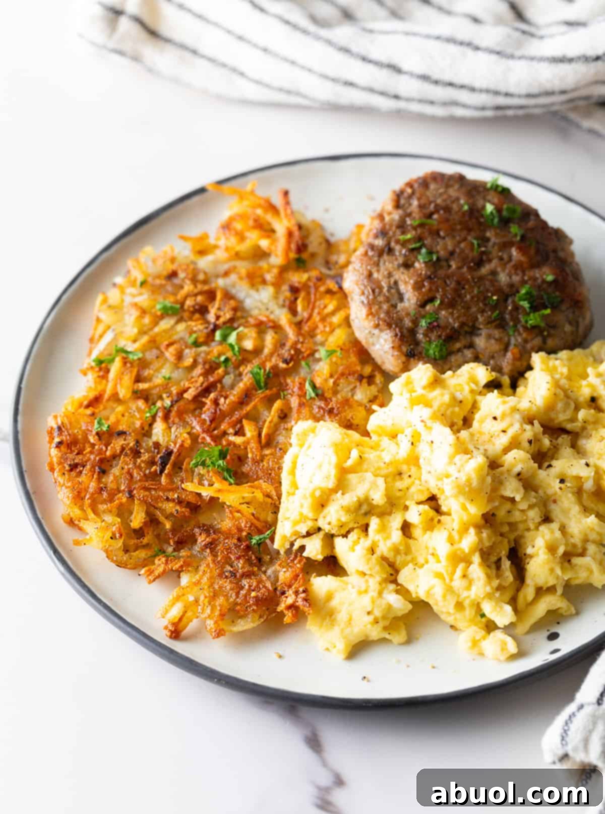 A white plate filled with homemade hash brown potatoes, breakfast sausage, and scrambled eggs. 
