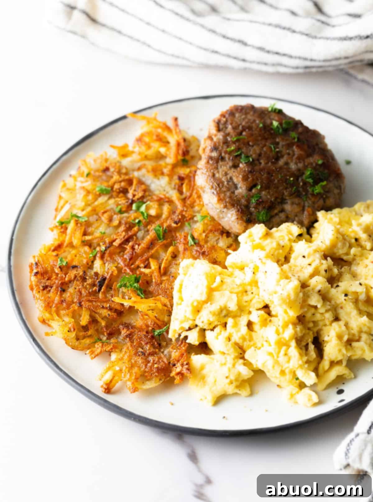 A white plate filled with homemade hash brown potatoes, breakfast sausage, and scrambled eggs.