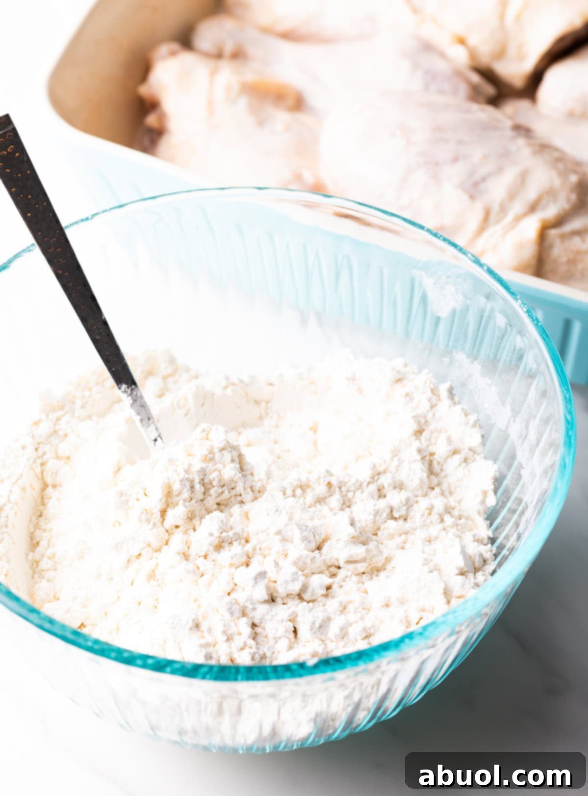 Southern Cast Iron Fried Chicken 7 A spoon mixing a flour, cornstarch, and salt mixture in a glass bowl for a deep fried chicken recipe.