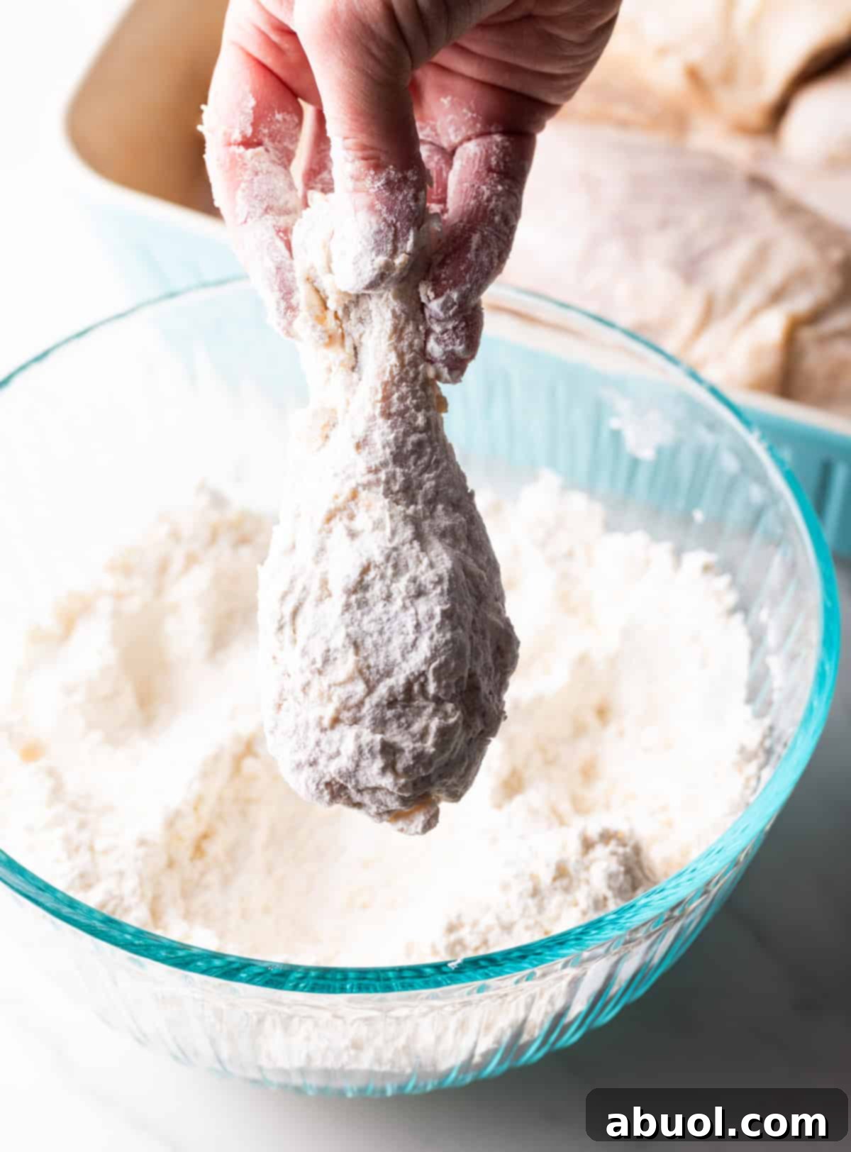 Southern Cast Iron Fried Chicken 8 A raw chicken wing being meticulously dredged in a seasoned flour mixture for Southern fried chicken.