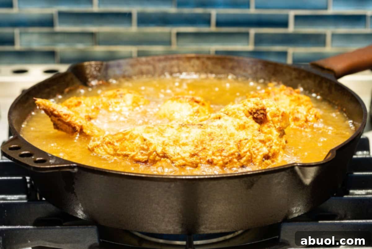 Southern Cast Iron Fried Chicken 9 Fried chicken pieces cooking to golden perfection in a cast-iron skillet filled with hot oil.